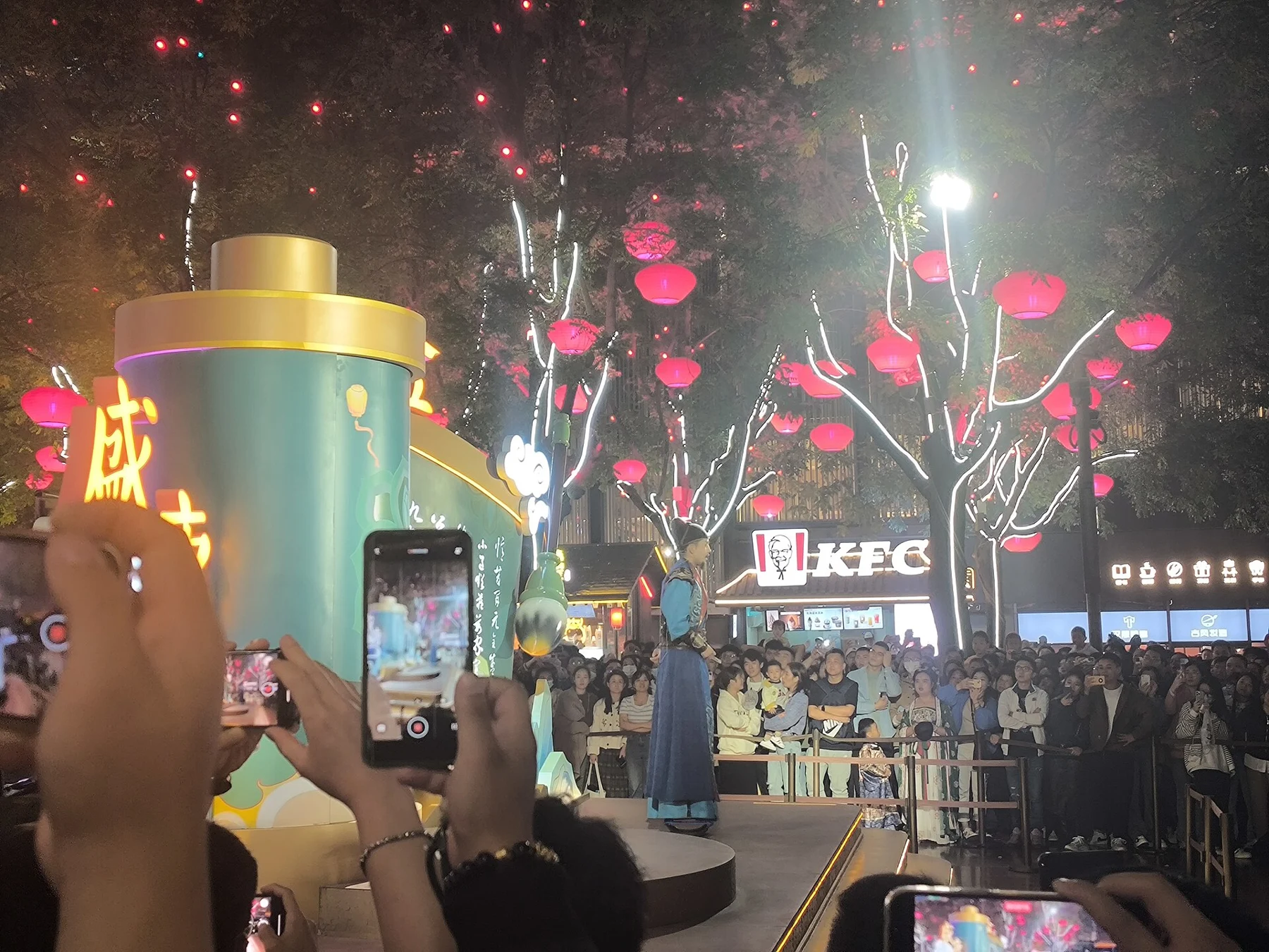 An audience watching costumed performers beside a cylindrical green stage prop.