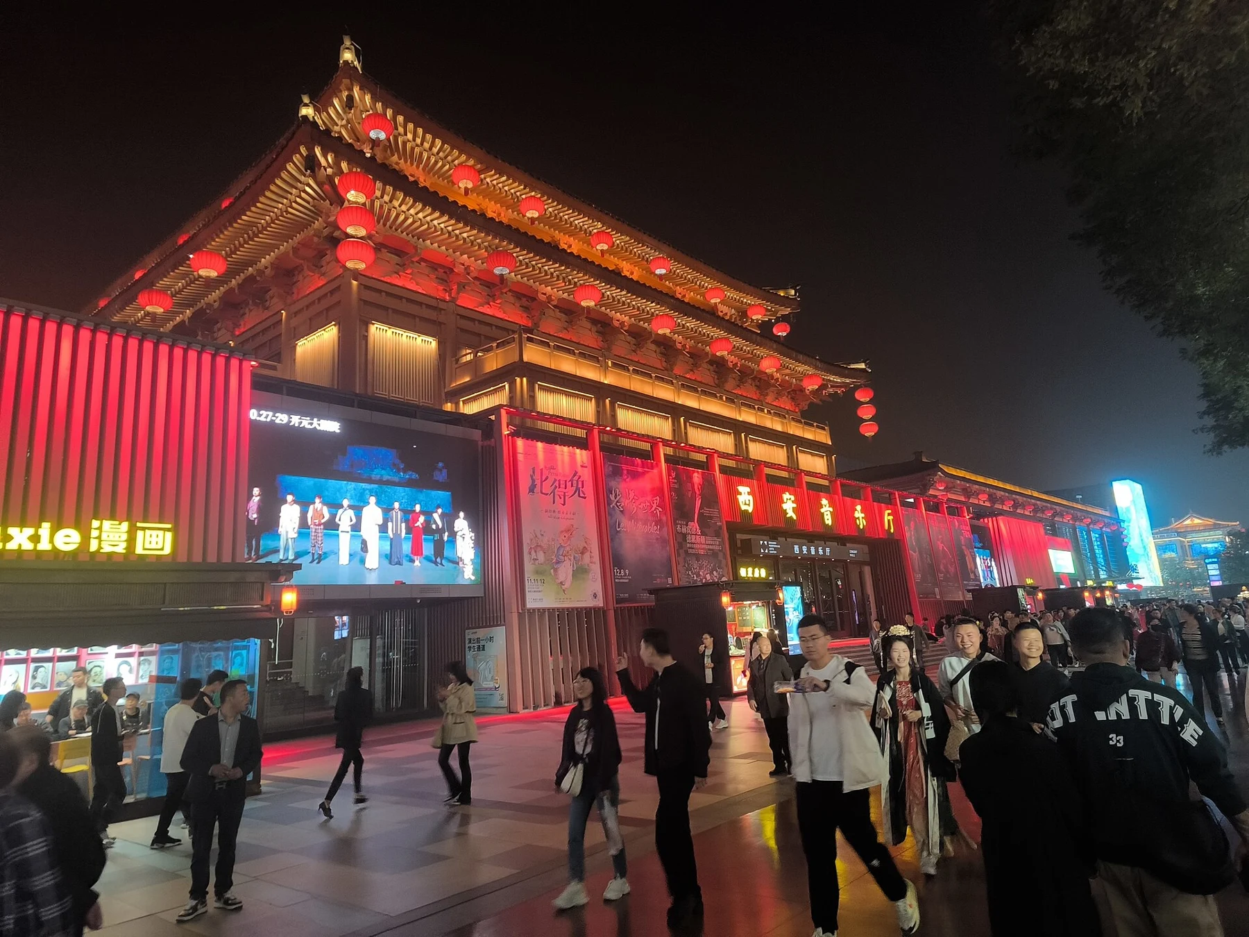 The 西安音乐厅 sign beneath an illuminated roof, with event posters and people in the street.