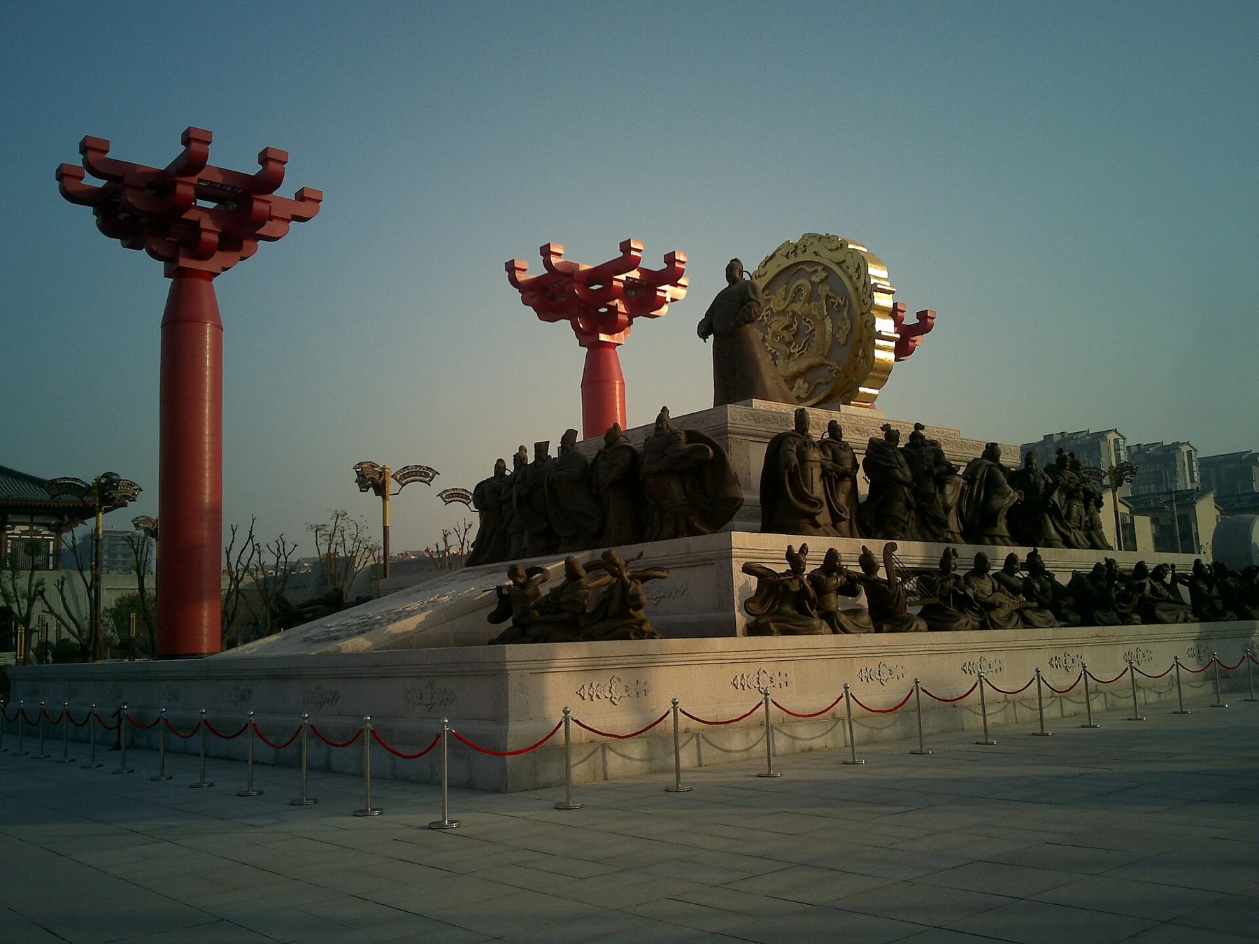 A tiered sculptural composition with human figures, a large round panel and red ornamental poles.