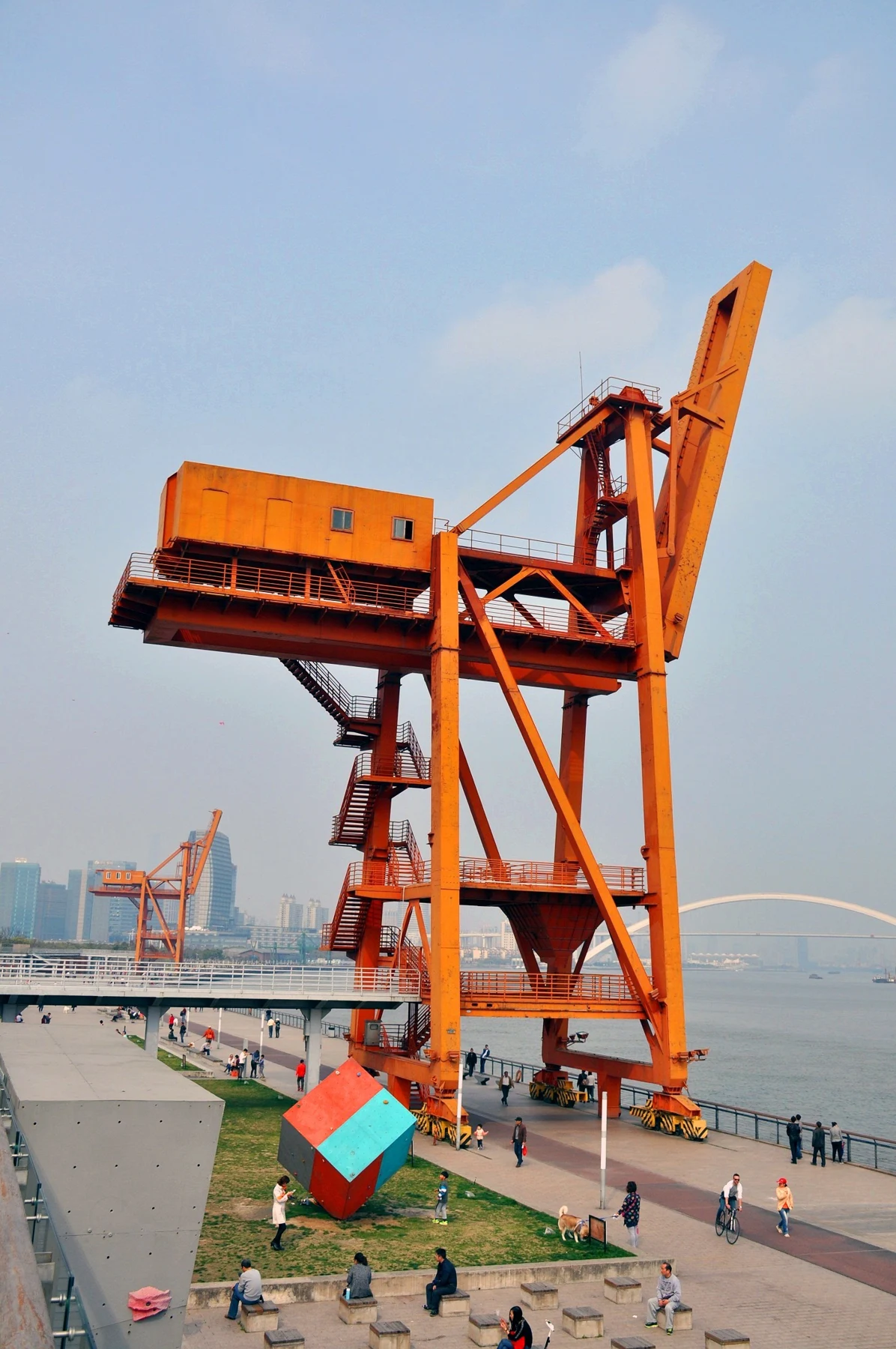 A tall orange port crane against a pale sky and riverside surroundings.