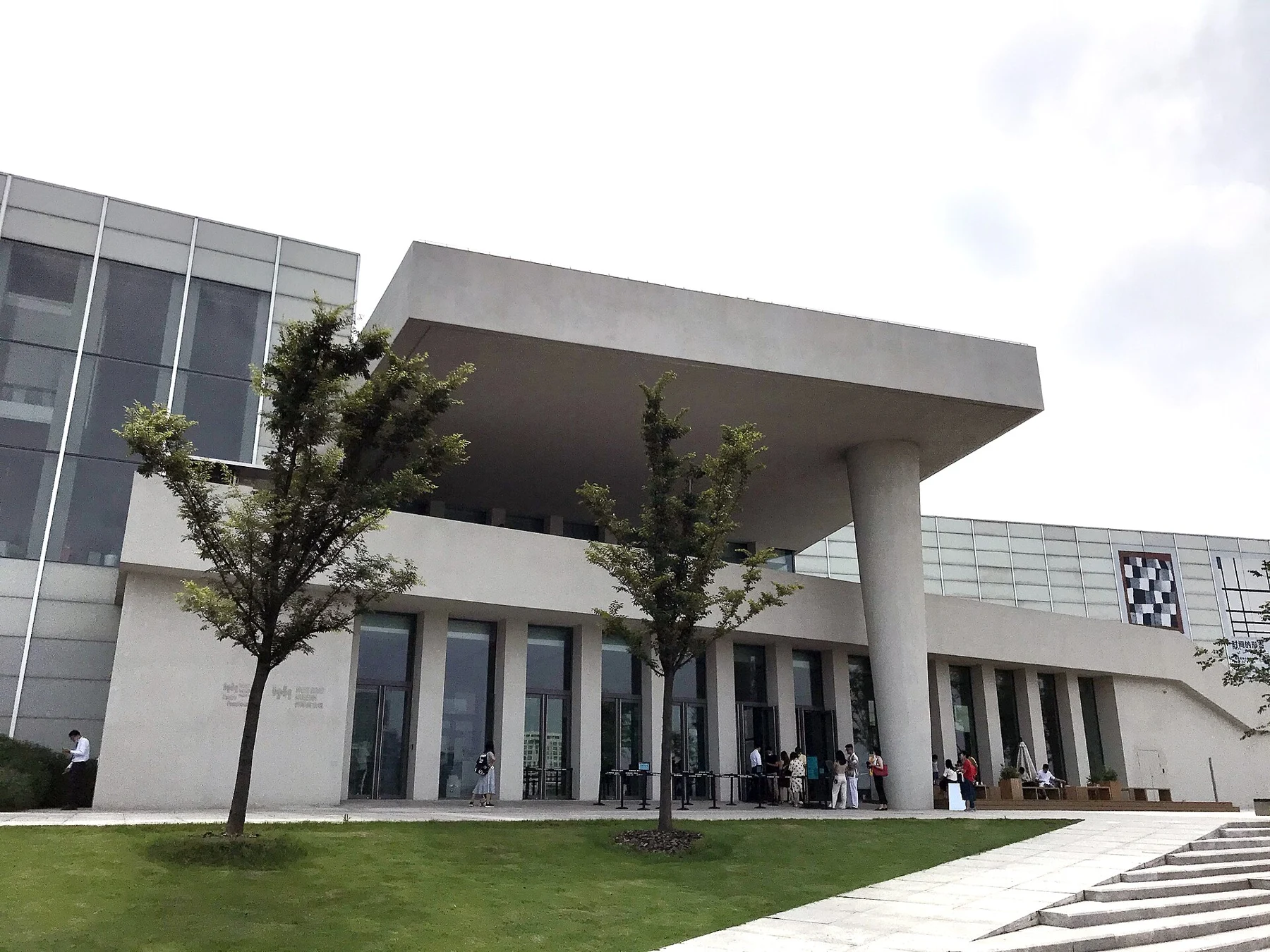An outdoor covered museum approach beneath large pale volumes.