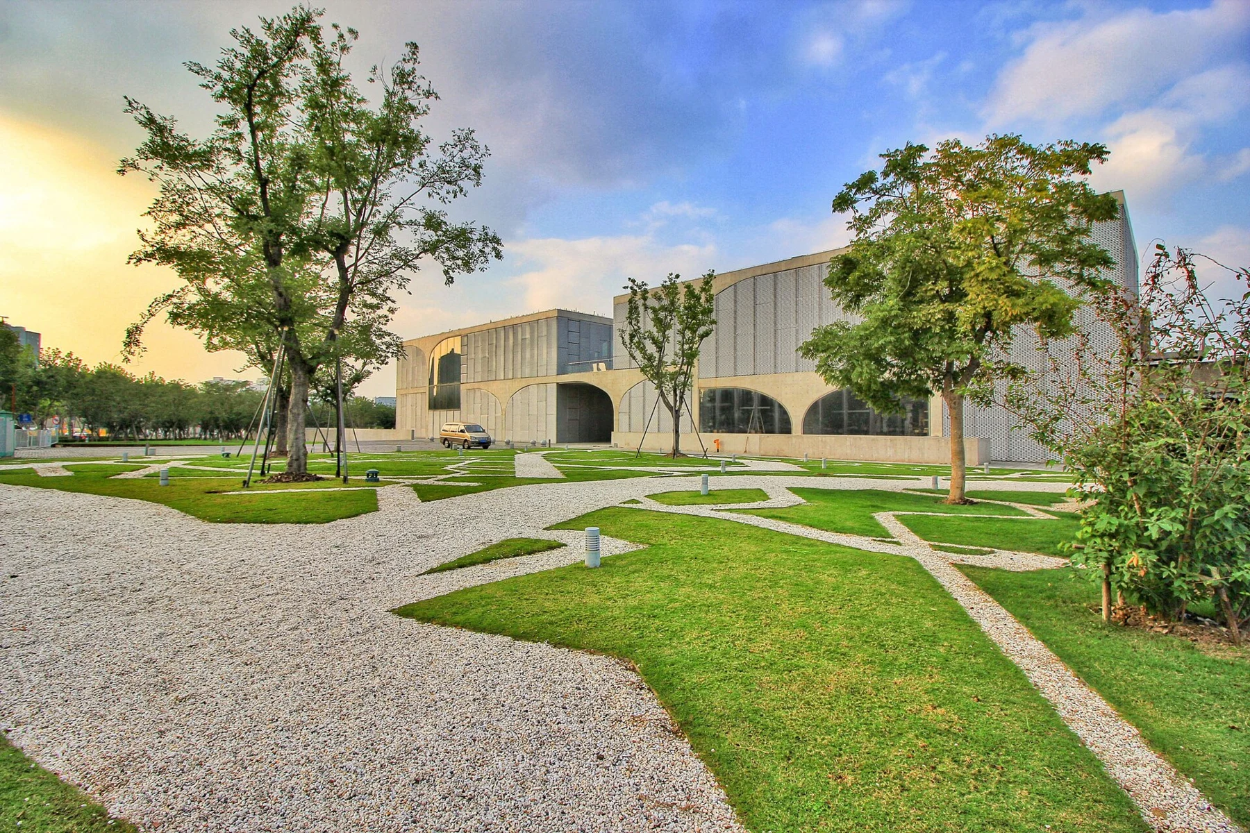 Paths, lawn and trees in front of a low building with curved concrete supports.
