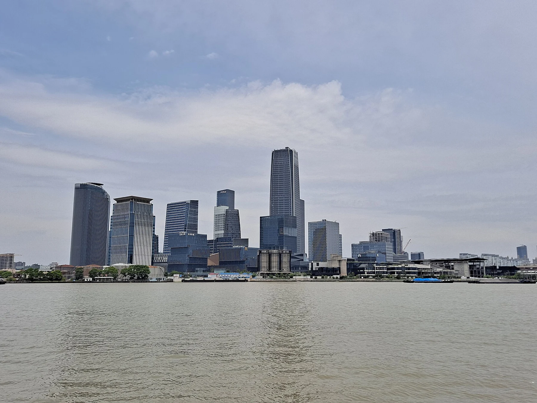 Modern towers beyond the river with a low planted embankment at the water’s edge.