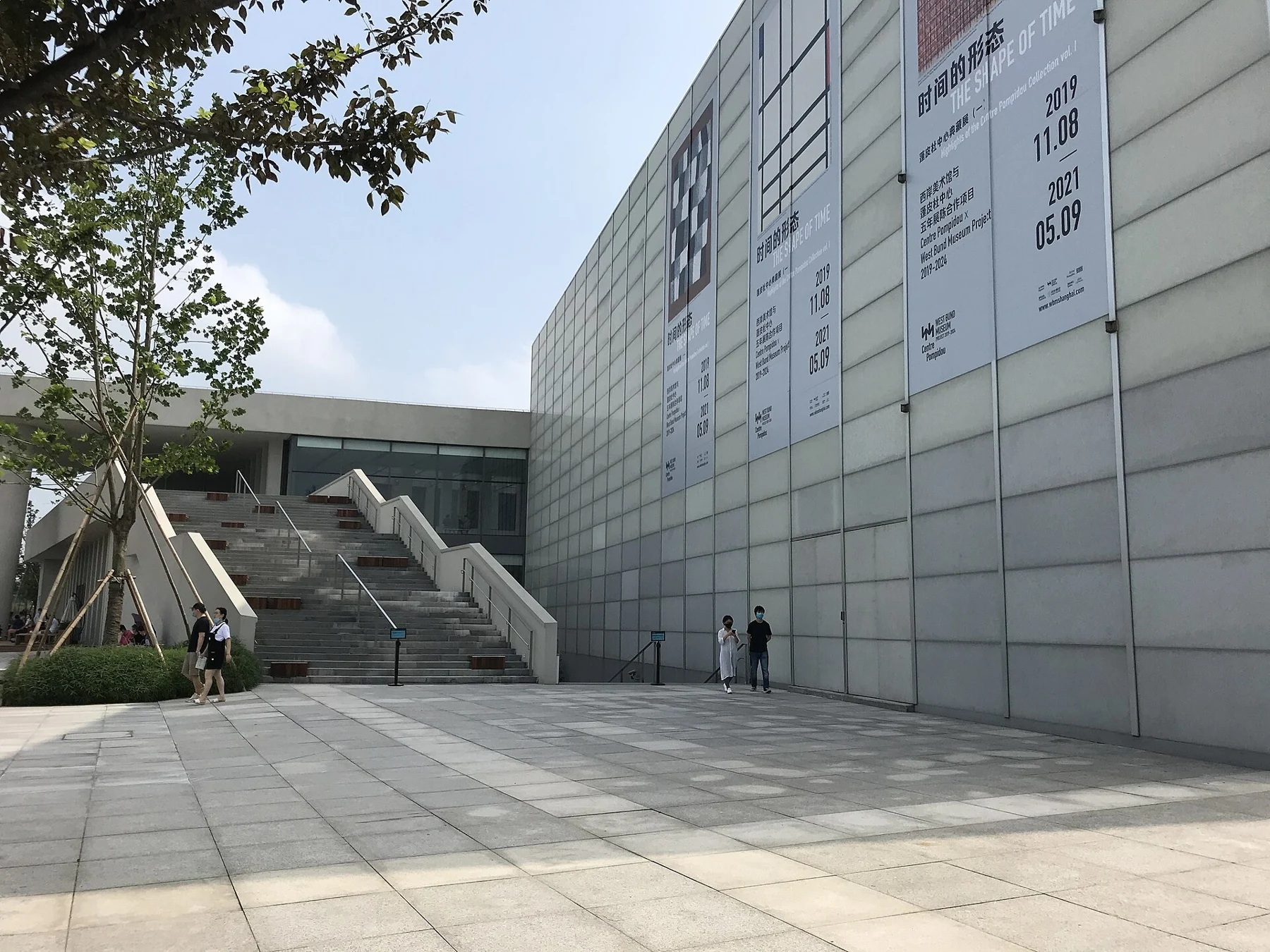 Broad steps below a pale glass-clad volume and old exhibition banner.