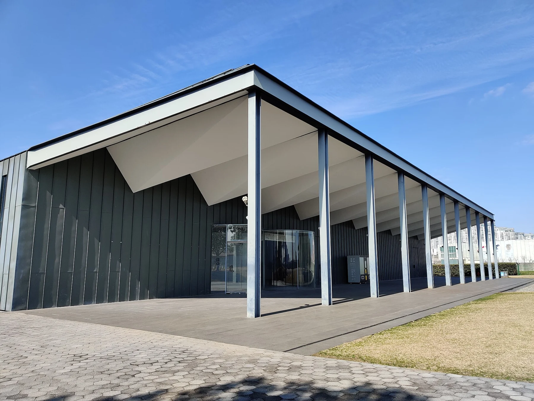 A compact glass-walled pavilion with a pale roof in an open landscape.