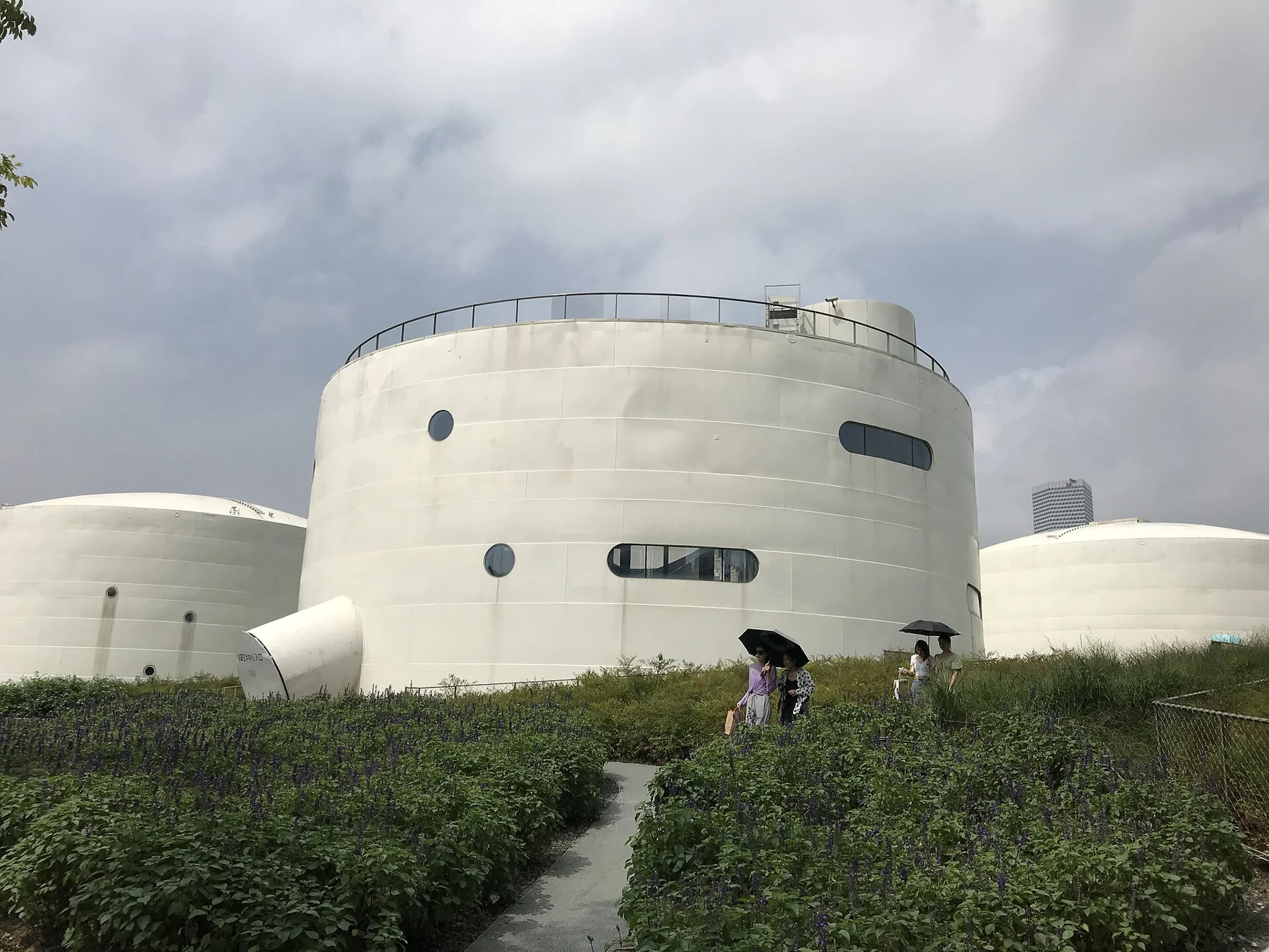 A cylindrical pale tank rising from a grassy mound.