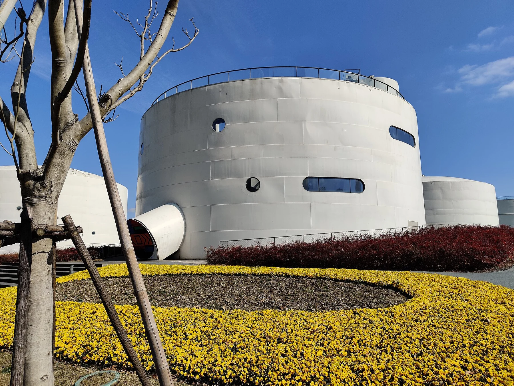 A pale circular tank with flowers and planted ground in the foreground.
