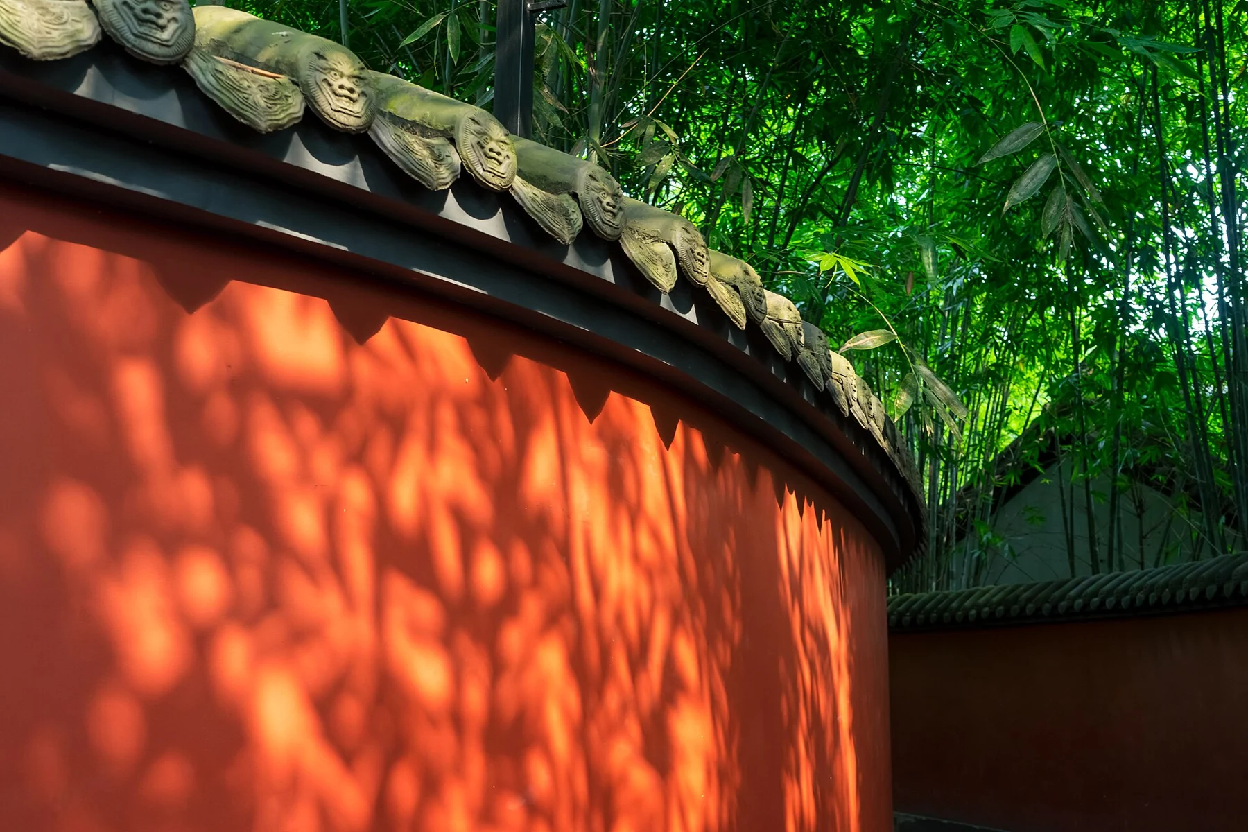 Sunlit red wall with dark bamboo shadows beneath a tiled cap
