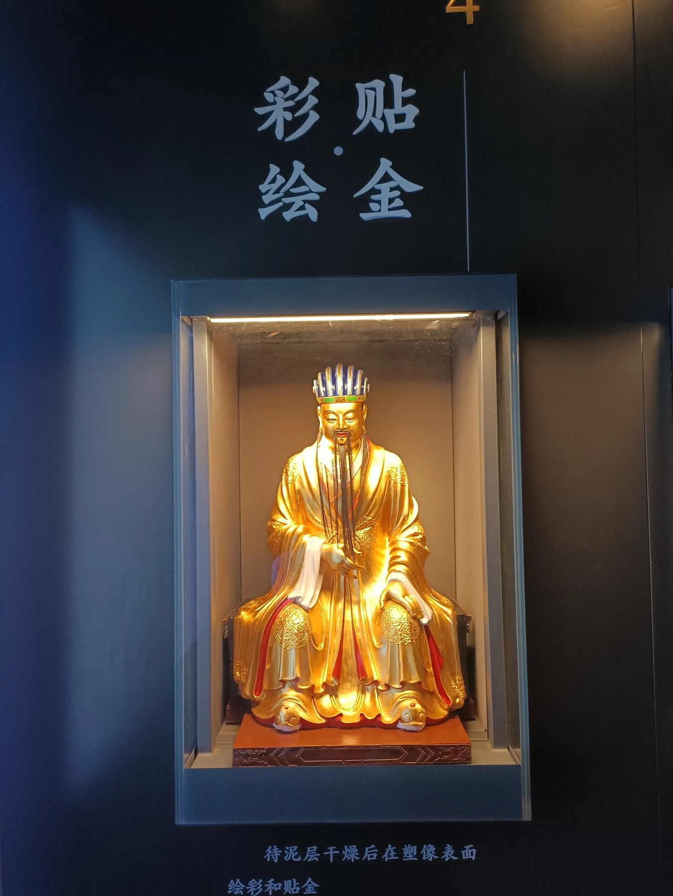 Small gilded seated figure in an exhibit about painting and gilding sculpture