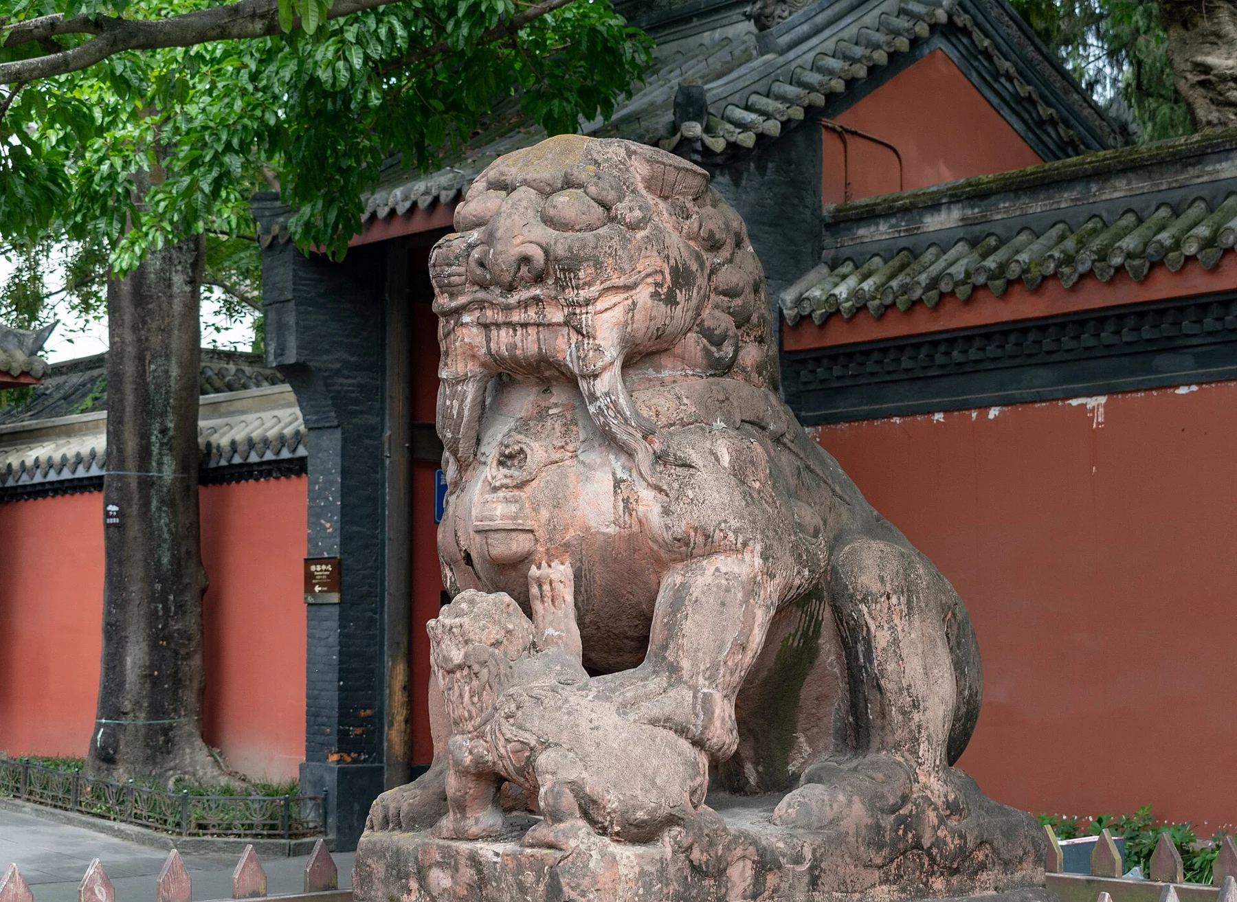 Weathered stone guardian lion on a pedestal beside a red wall