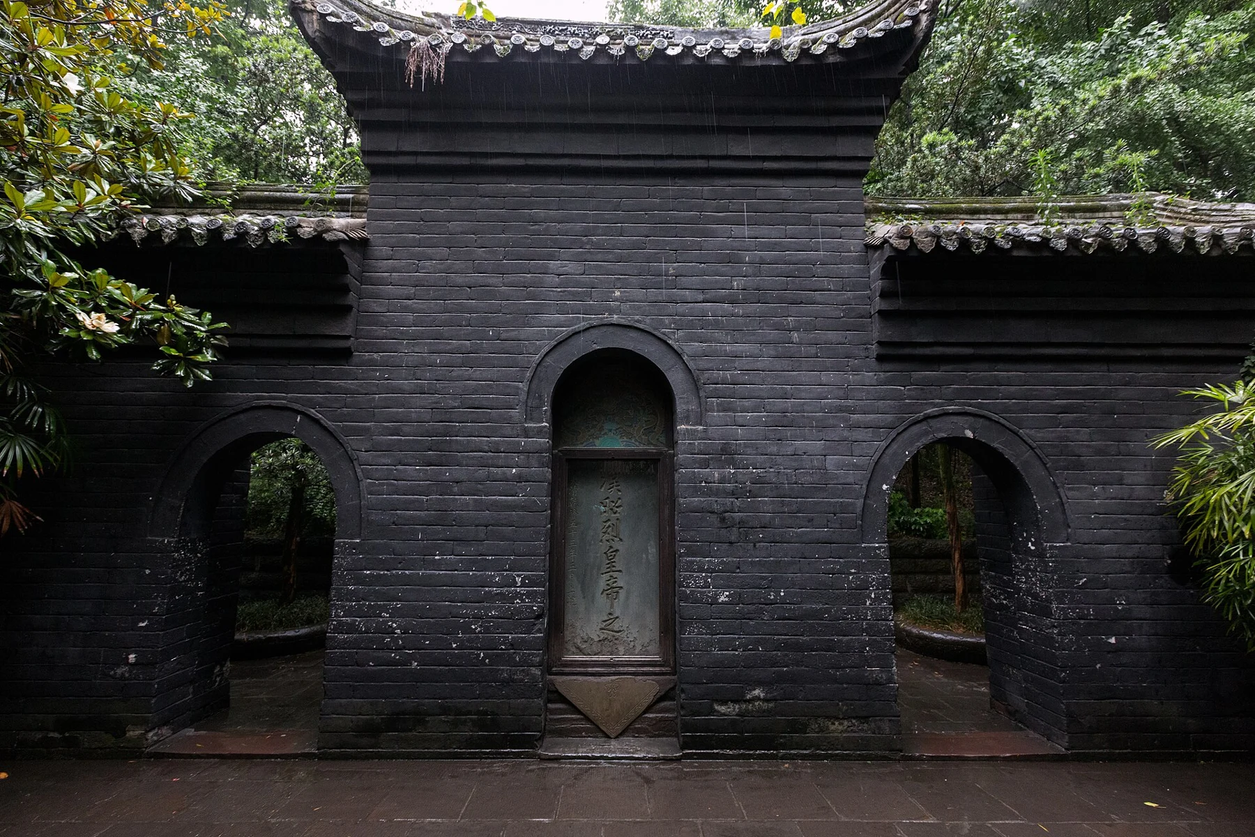 Brick memorial wall with a central inscribed stone and two arched side passages
