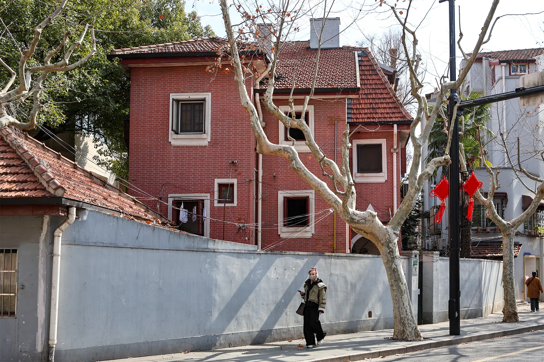 A red-painted house with white trim, tiled roofs and a pale wall along the pavement.