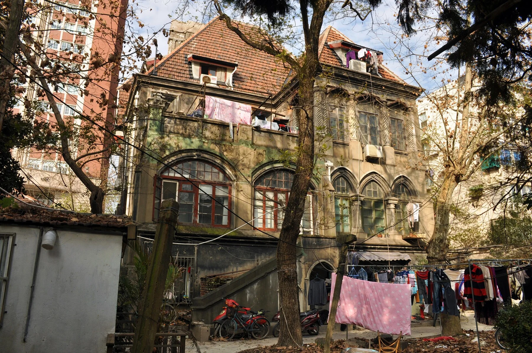 A weathered house with a tiled roof, arched windows, exterior steps and hanging laundry.
