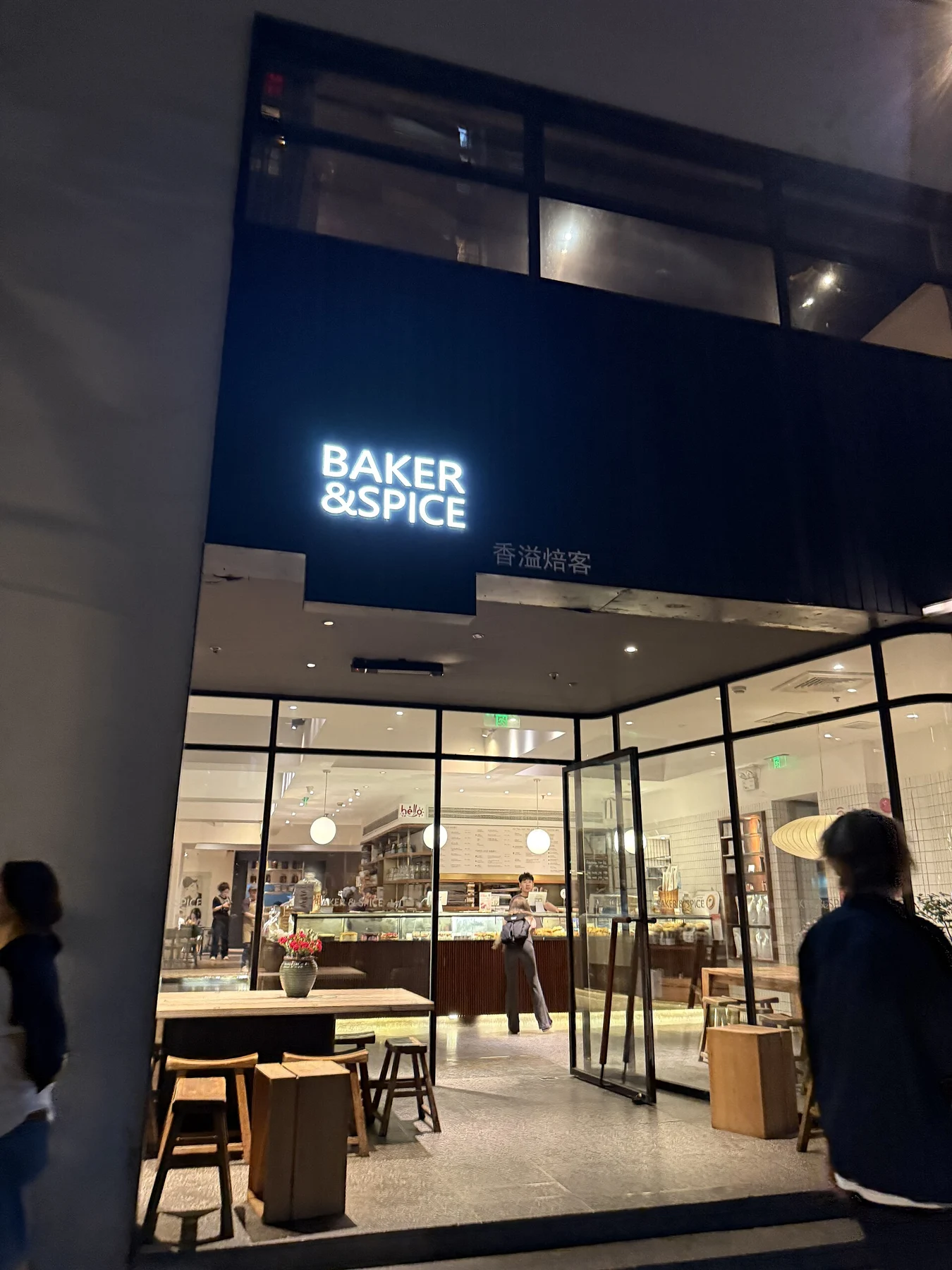 A lit café frontage with a Baker & Spice sign above street-side tables.
