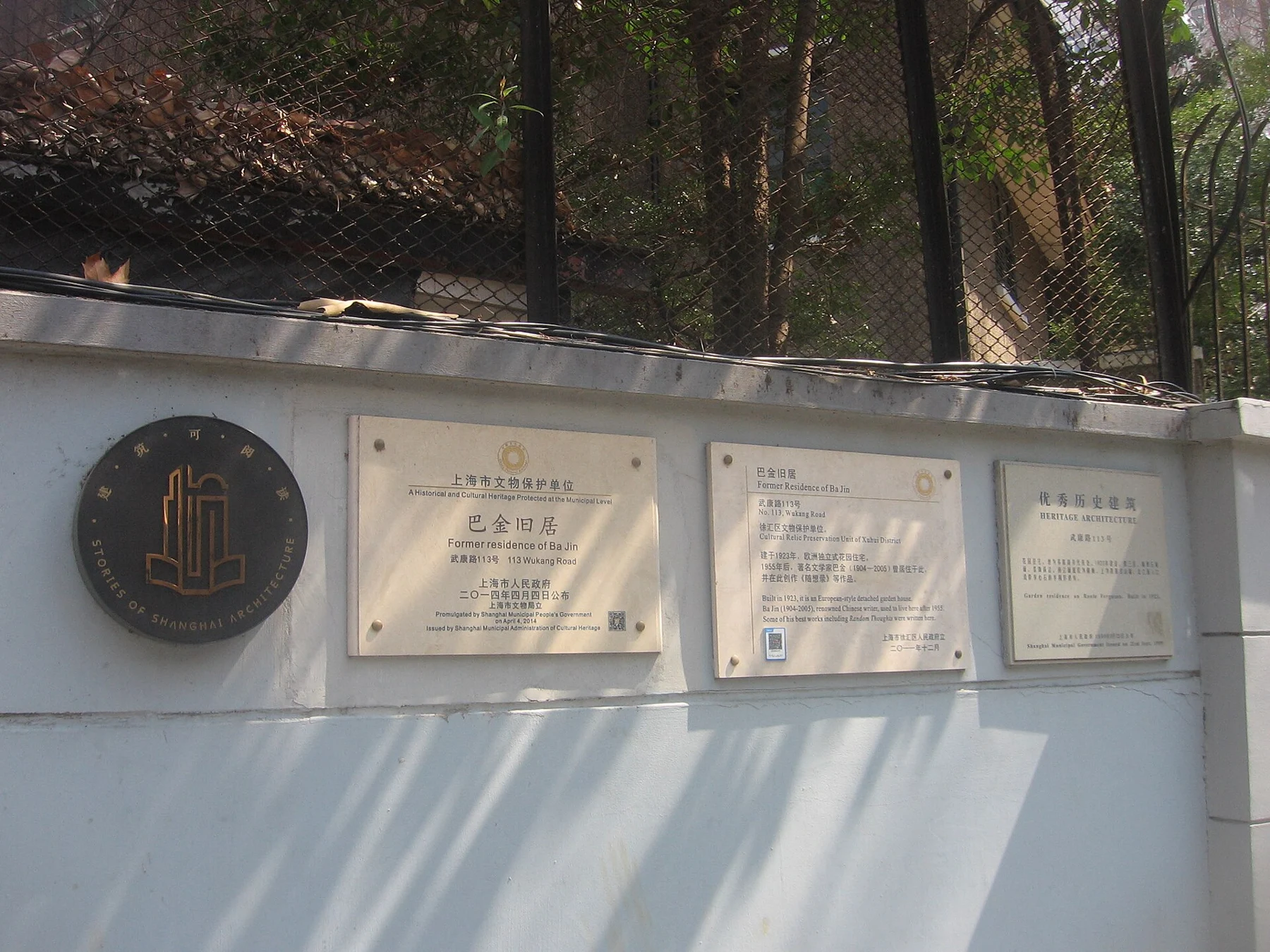 Heritage plaques on a pale boundary wall beneath wire mesh and foliage.