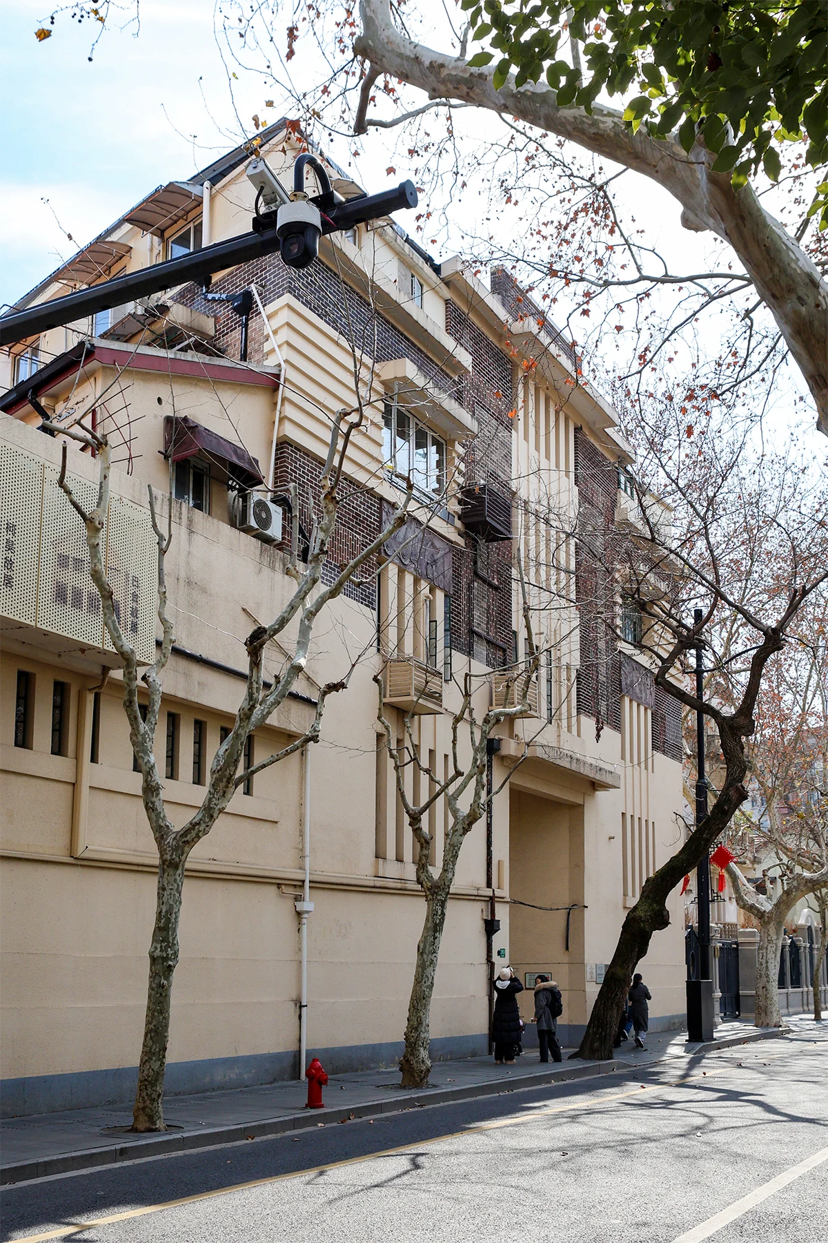 A pale street-facing building with roof dormers, external pipes and trees in front.