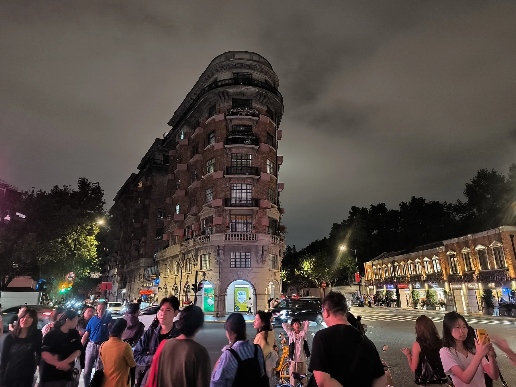Wukang Building after dark with groups of people waiting by the street corner.