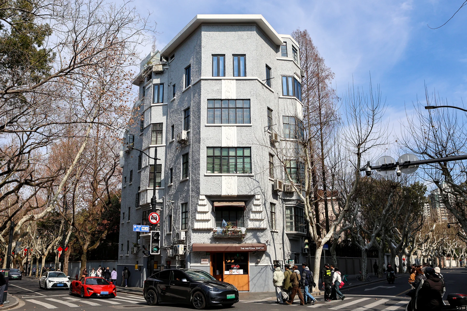 A compact pale-grey corner apartment building with projecting geometric and curved details.