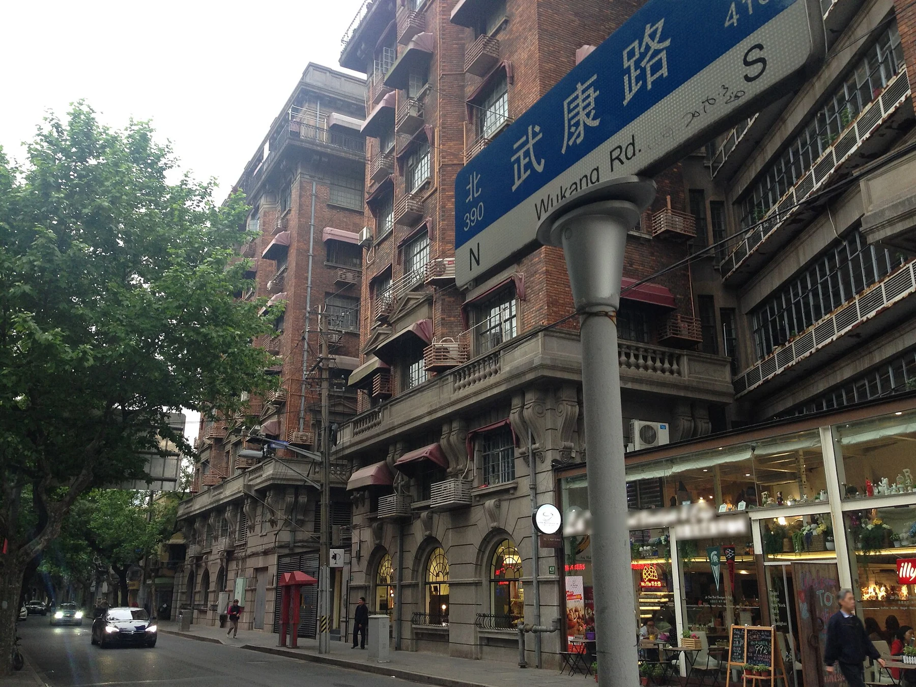 A blue 武康路 Wukang Road street sign in front of the long apartment façade.
