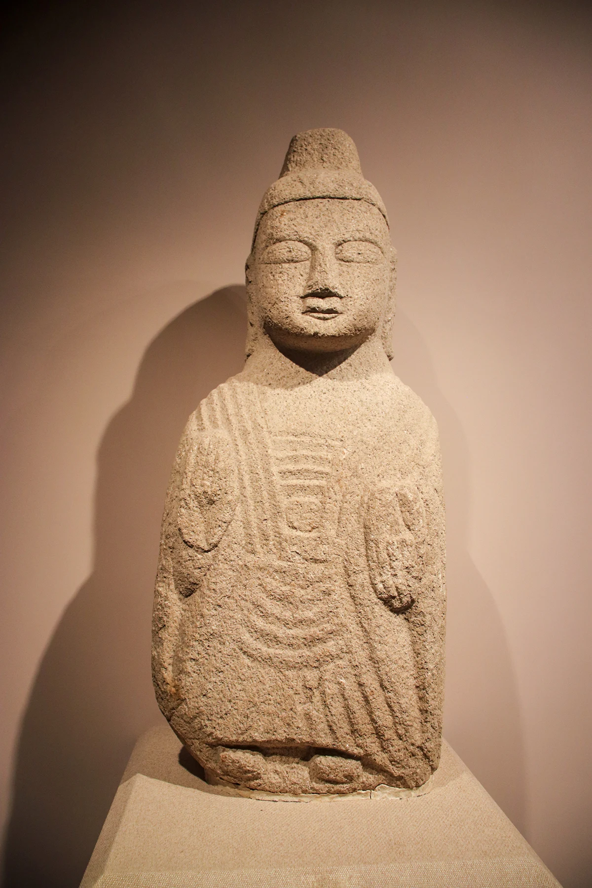 A weathered standing stone Buddhist figure with a high headdress and carved drapery.
