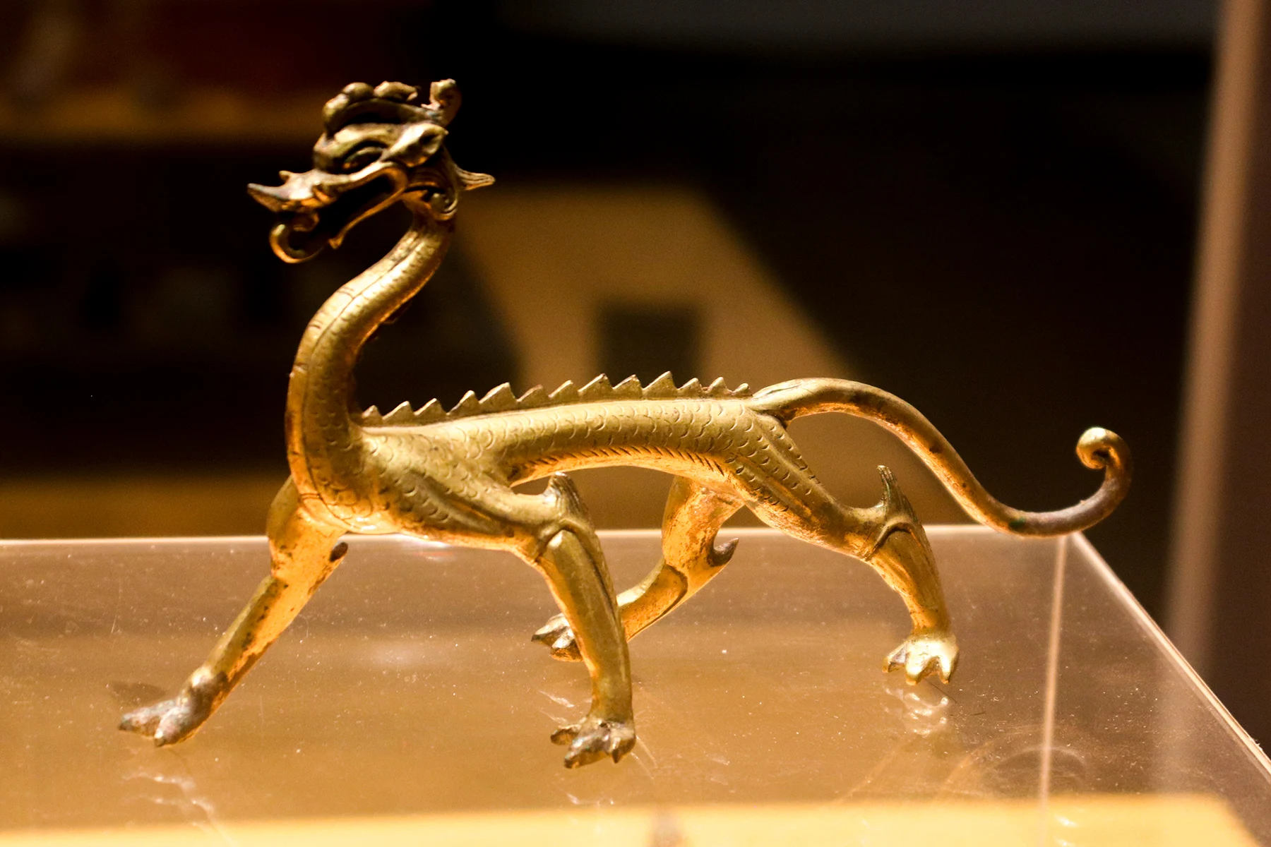 A small gilt dragon with an open mouth, raised spine and four striding legs.