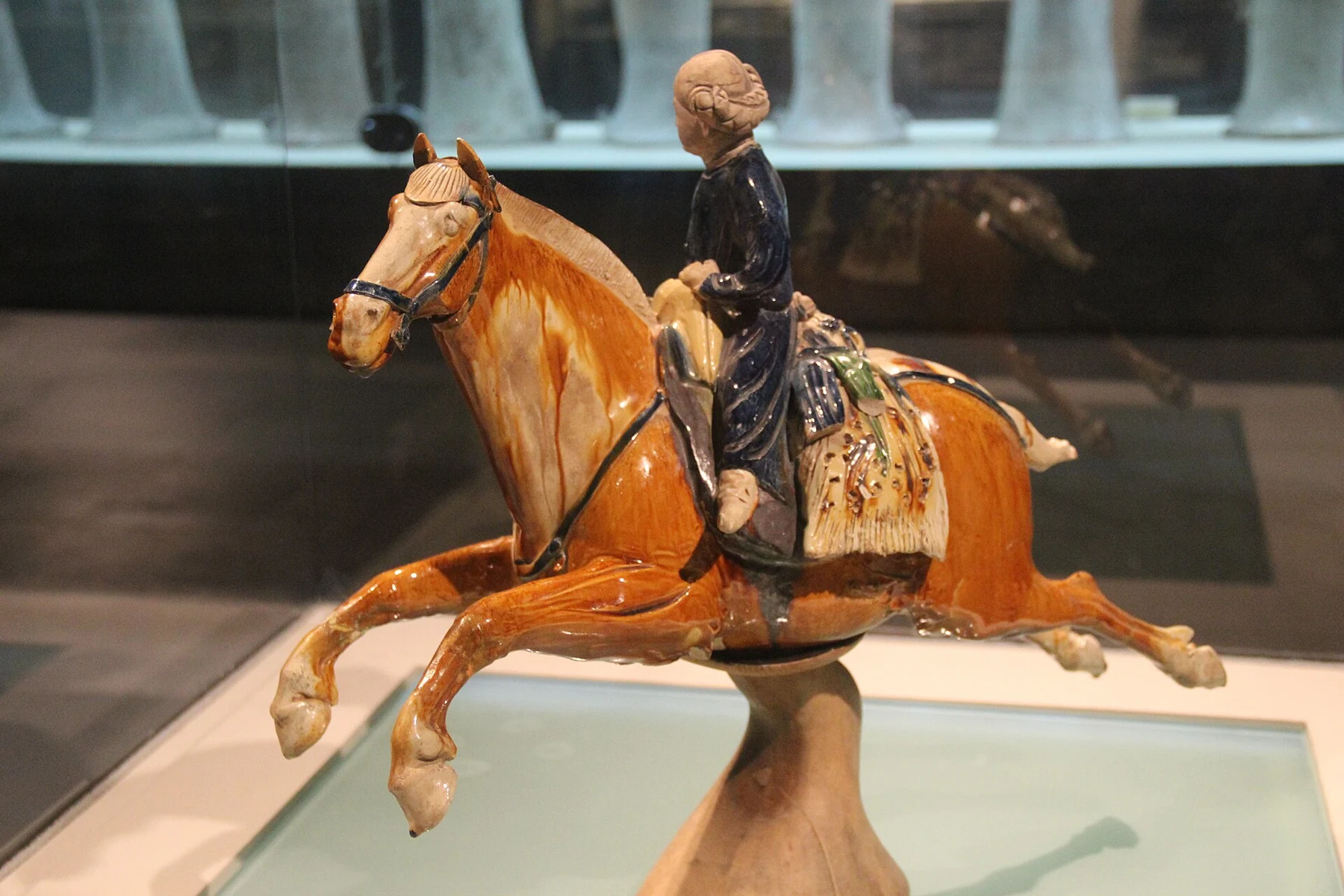 A close side view of the horse’s stretched legs, blue-coated rider and rear saddle bag.