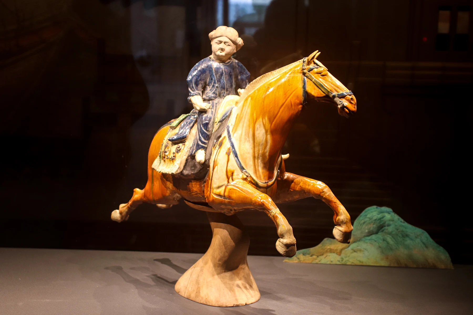 The glazed orange-brown galloping horse with a blue-robed rider and a support beneath it.