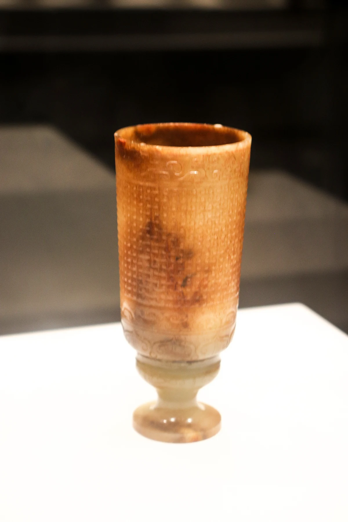 A tall brown-toned jade cup with carved surface bands and a pale high foot.