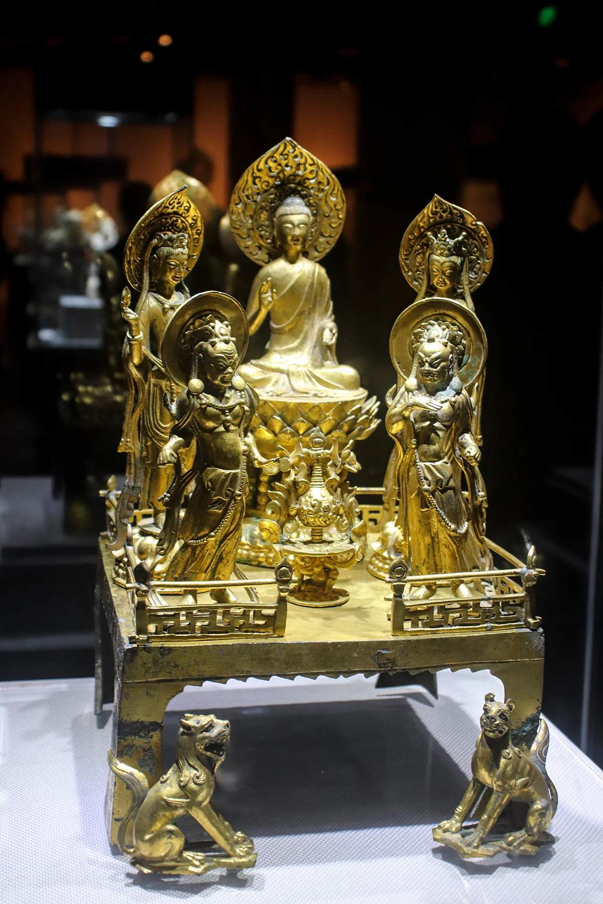 A central seated Buddha flanked by two standing figures with decorated haloes and smaller figures below.