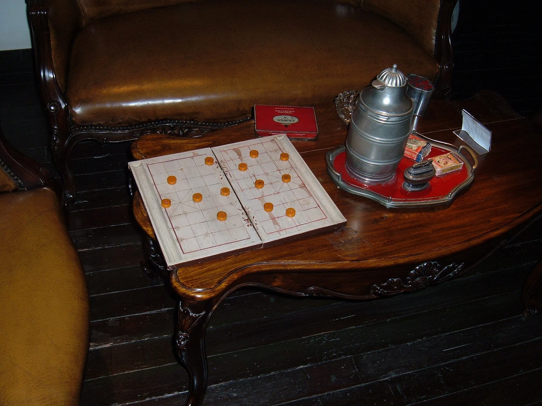 A historical display with a wooden seat, board game, a flask and stacked metal food containers.