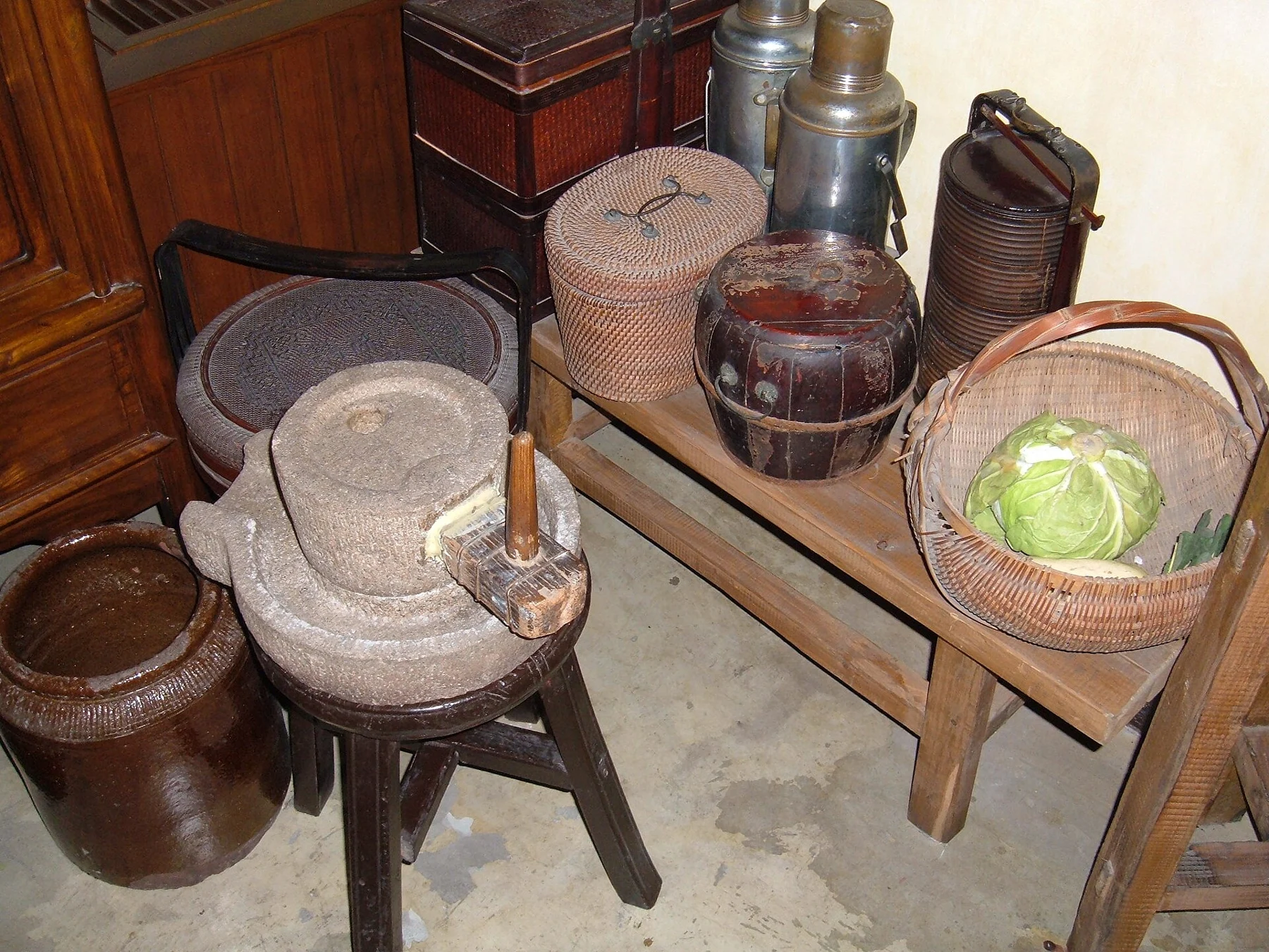 A historical kitchen display with ceramic containers, baskets, a bowl and vegetables.