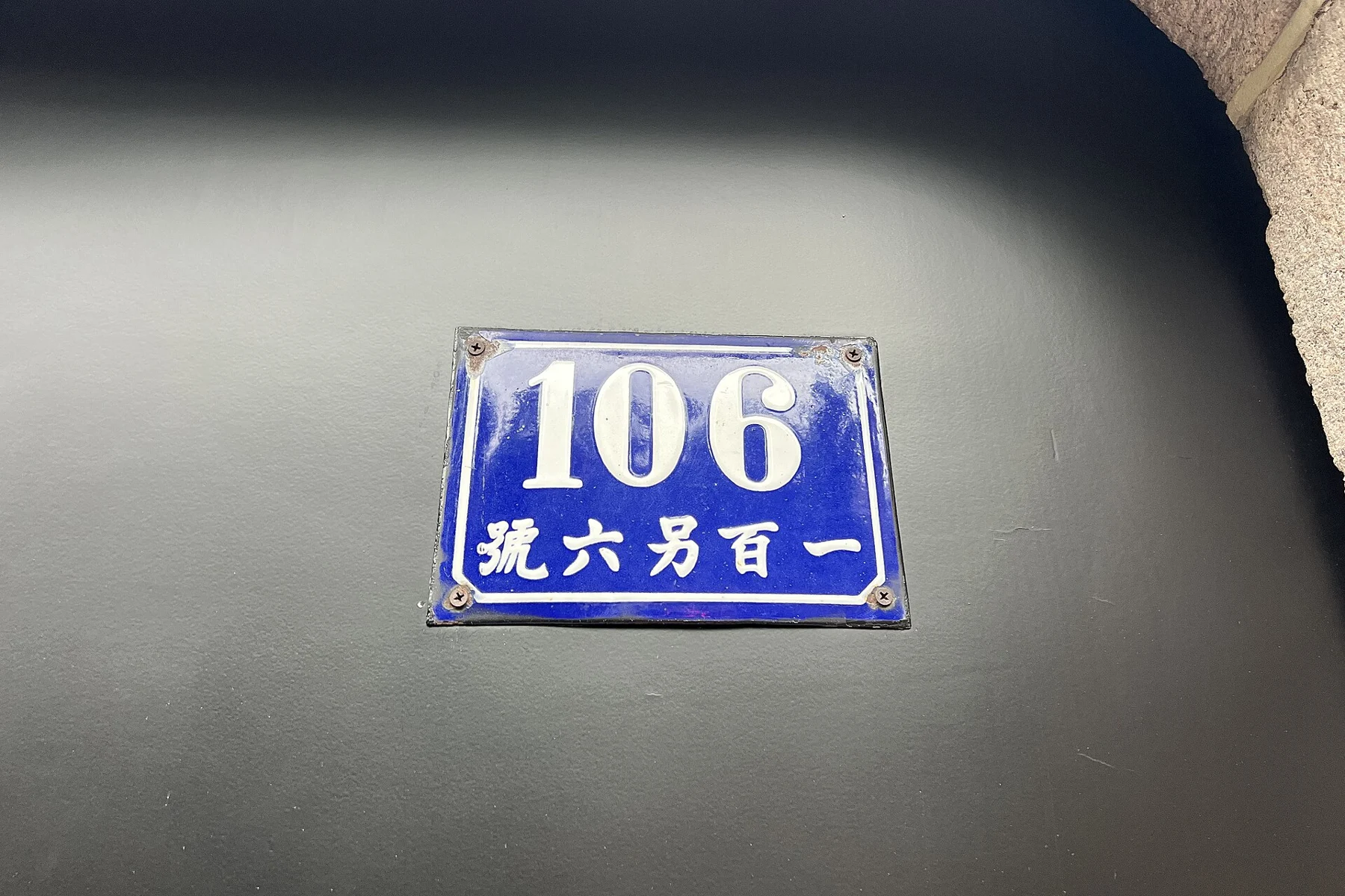 A blue enamel number 106 sign mounted on a pale wall.