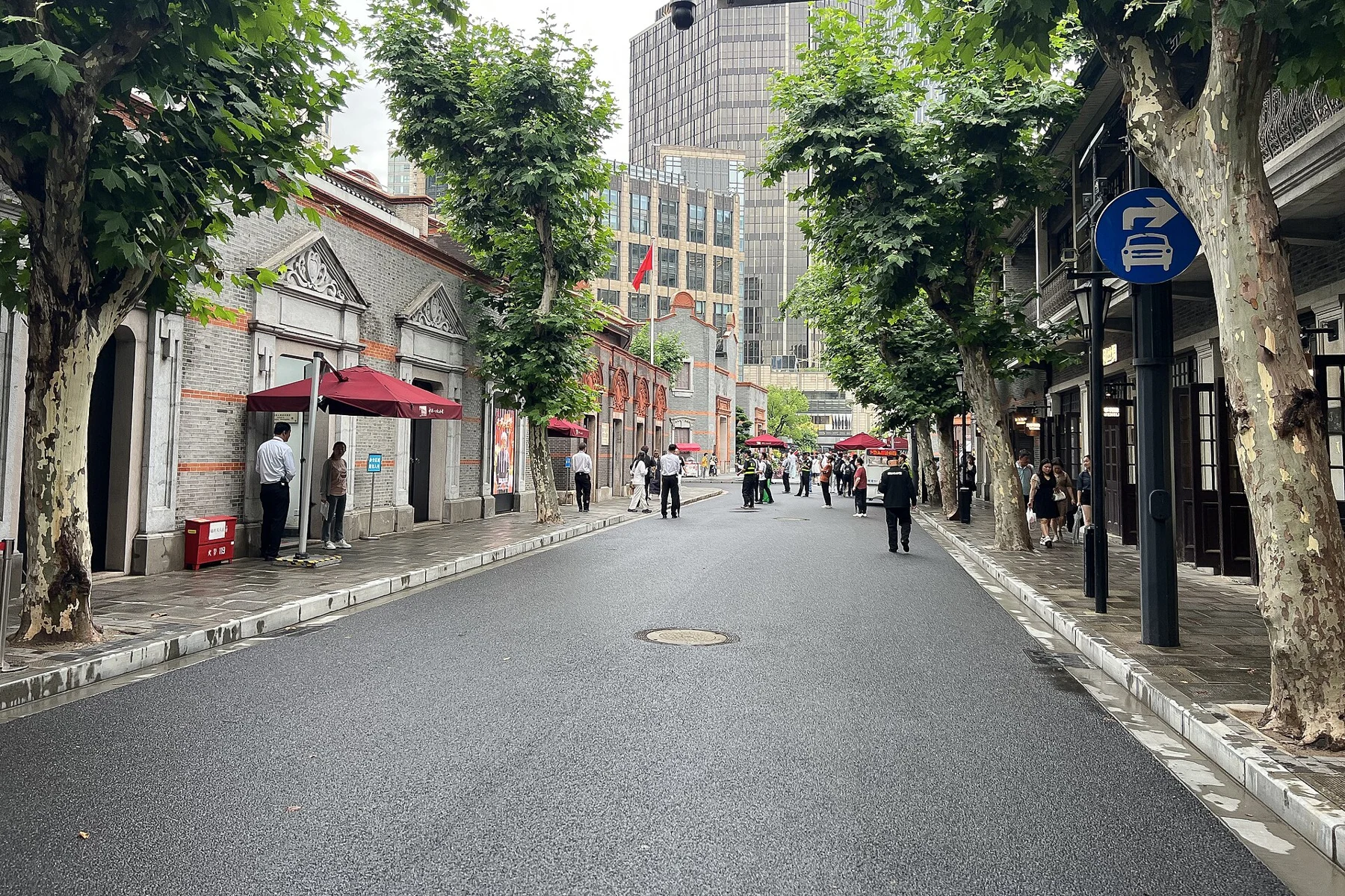 A tree-lined street with pedestrians, a low historic façade and modern buildings beyond.
