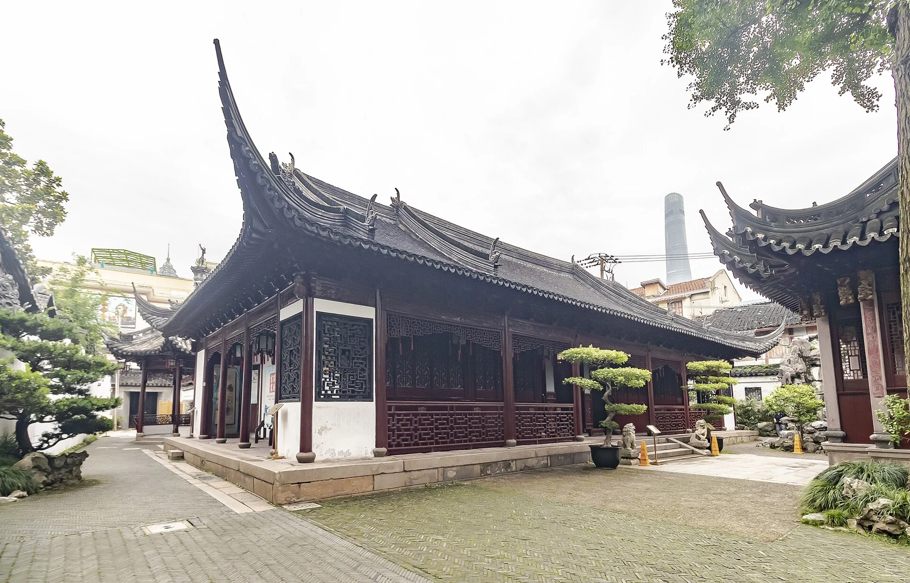 A timber hall with long eaves and red doors beside a paved courtyard.