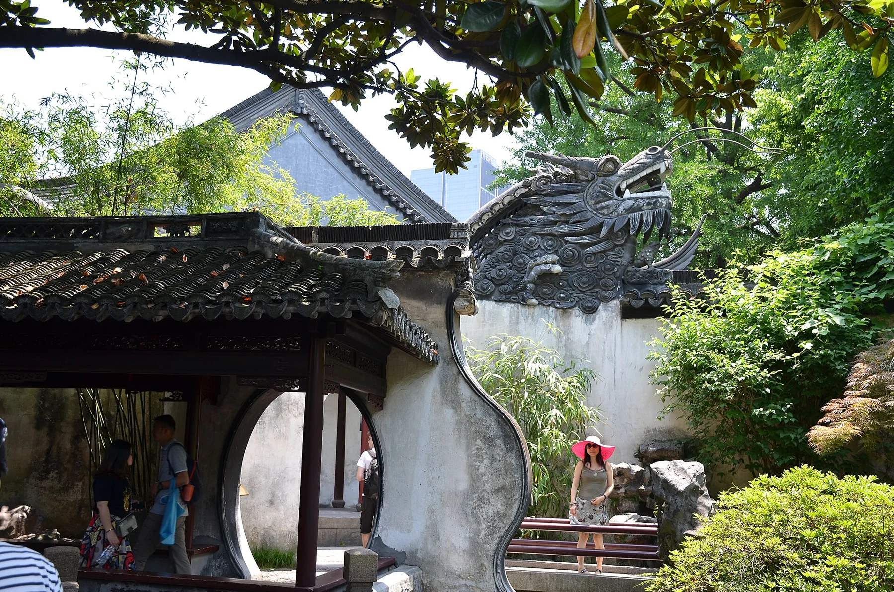 A white gateway wall with tiled dragon ornament and leafy trees behind it.