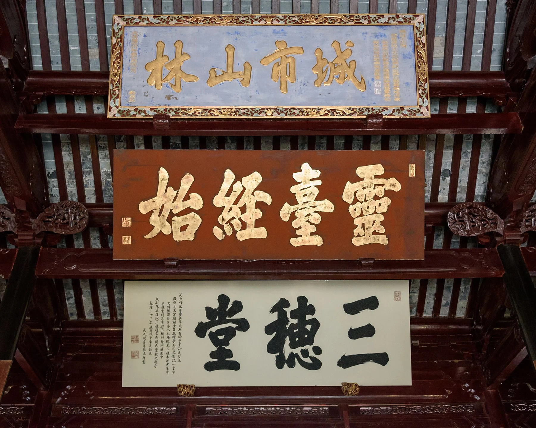 Three Chinese inscribed plaques beneath the dark timber rafters of a hall.
