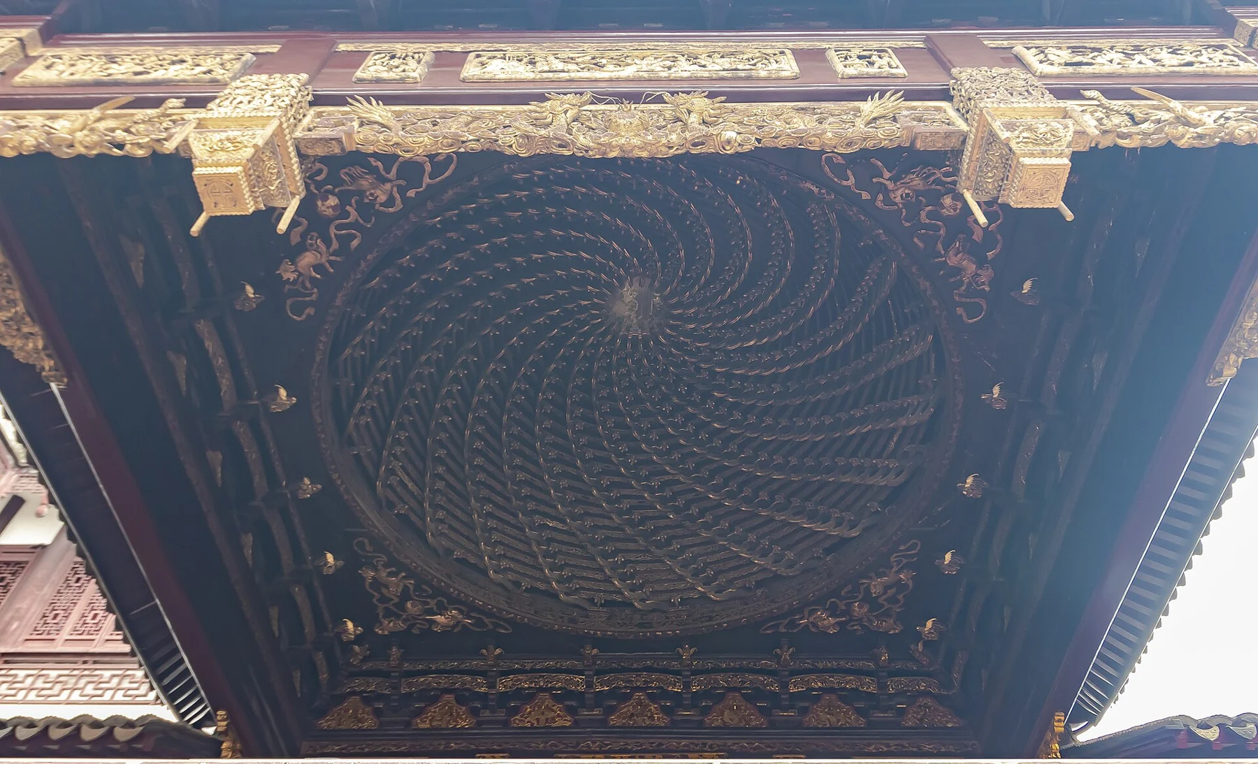 A richly carved circular spiral of timber under the stage roof, framed by gilded ornament.