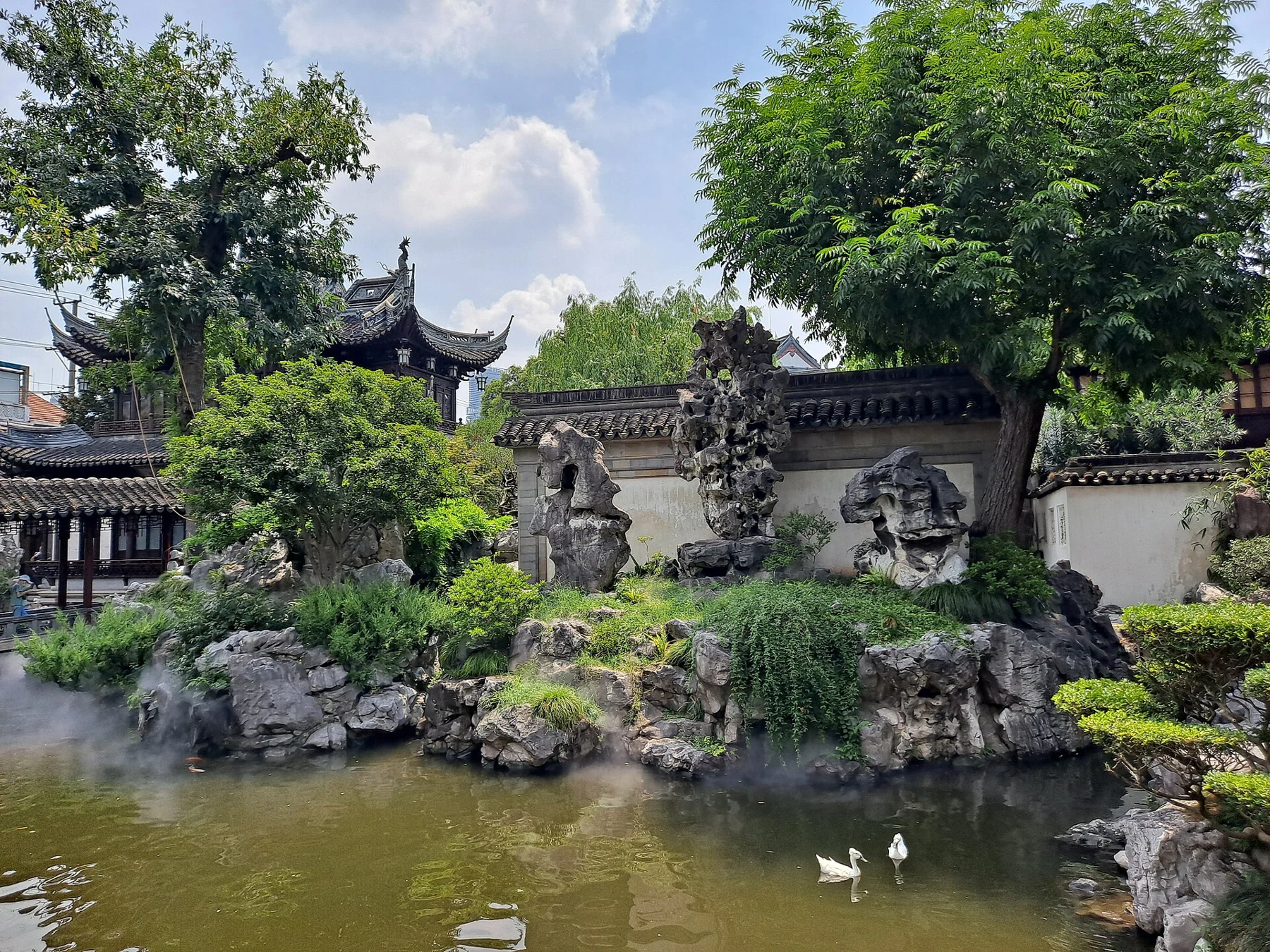 A tall pierced ornamental rock above a pond, flanked by smaller rocks and a patterned wall.