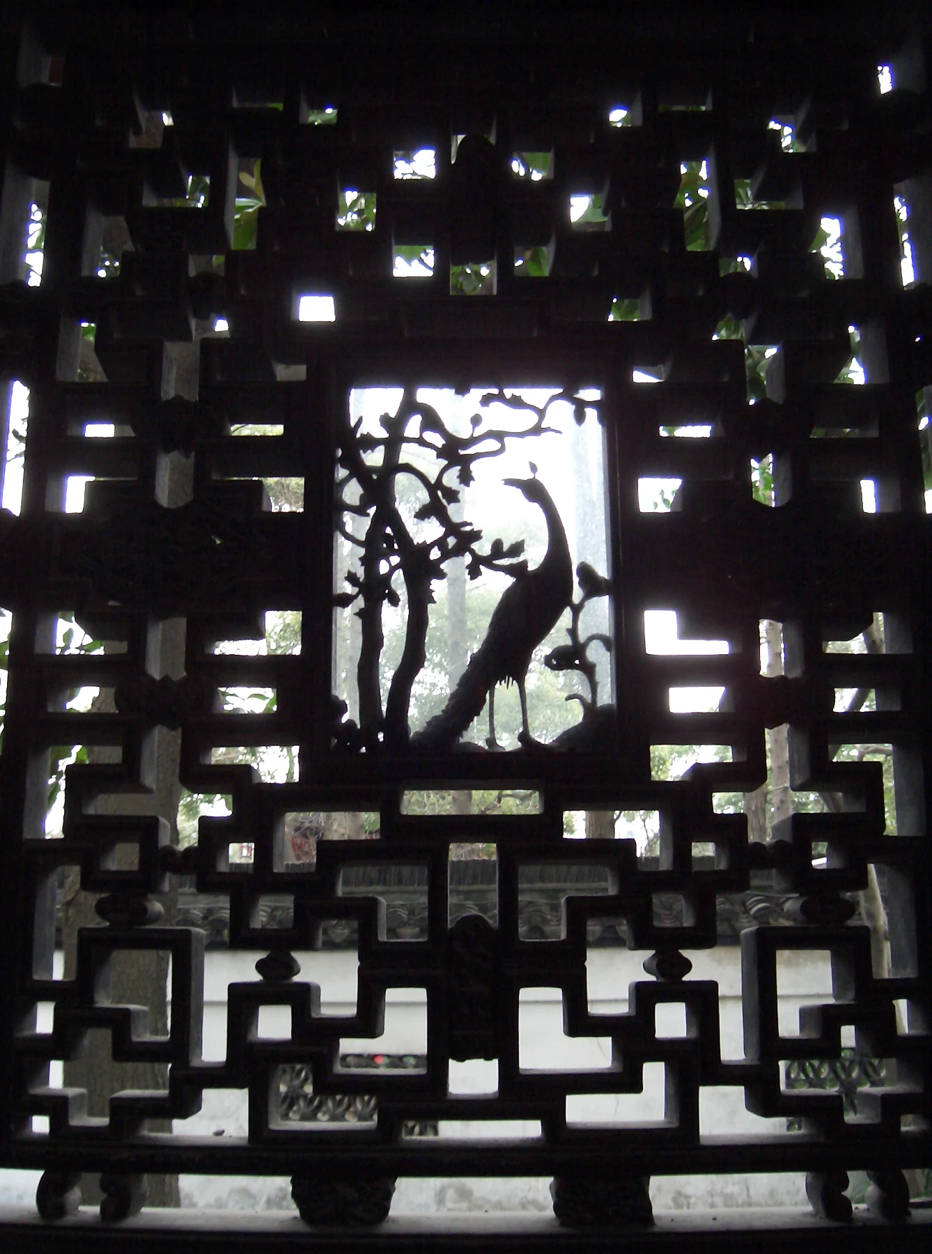 A dark openwork window with a bird in a circular central pattern and geometric openings around it.