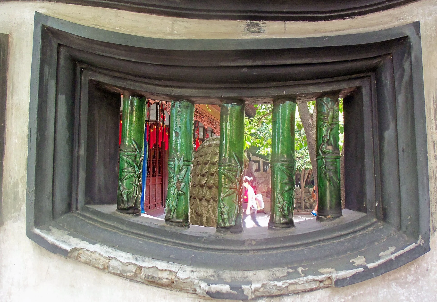 A curved recessed window fitted with green bars shaped like bamboo stems.