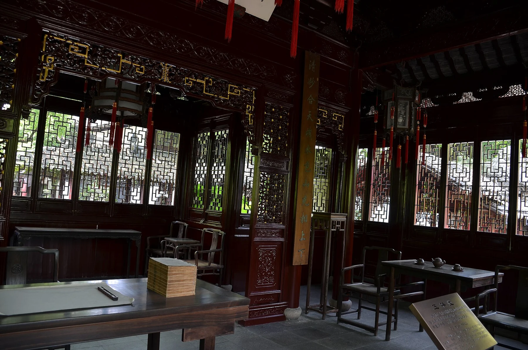 Dark timber furnishings, tables, chairs and carved panels in a shaded garden hall.