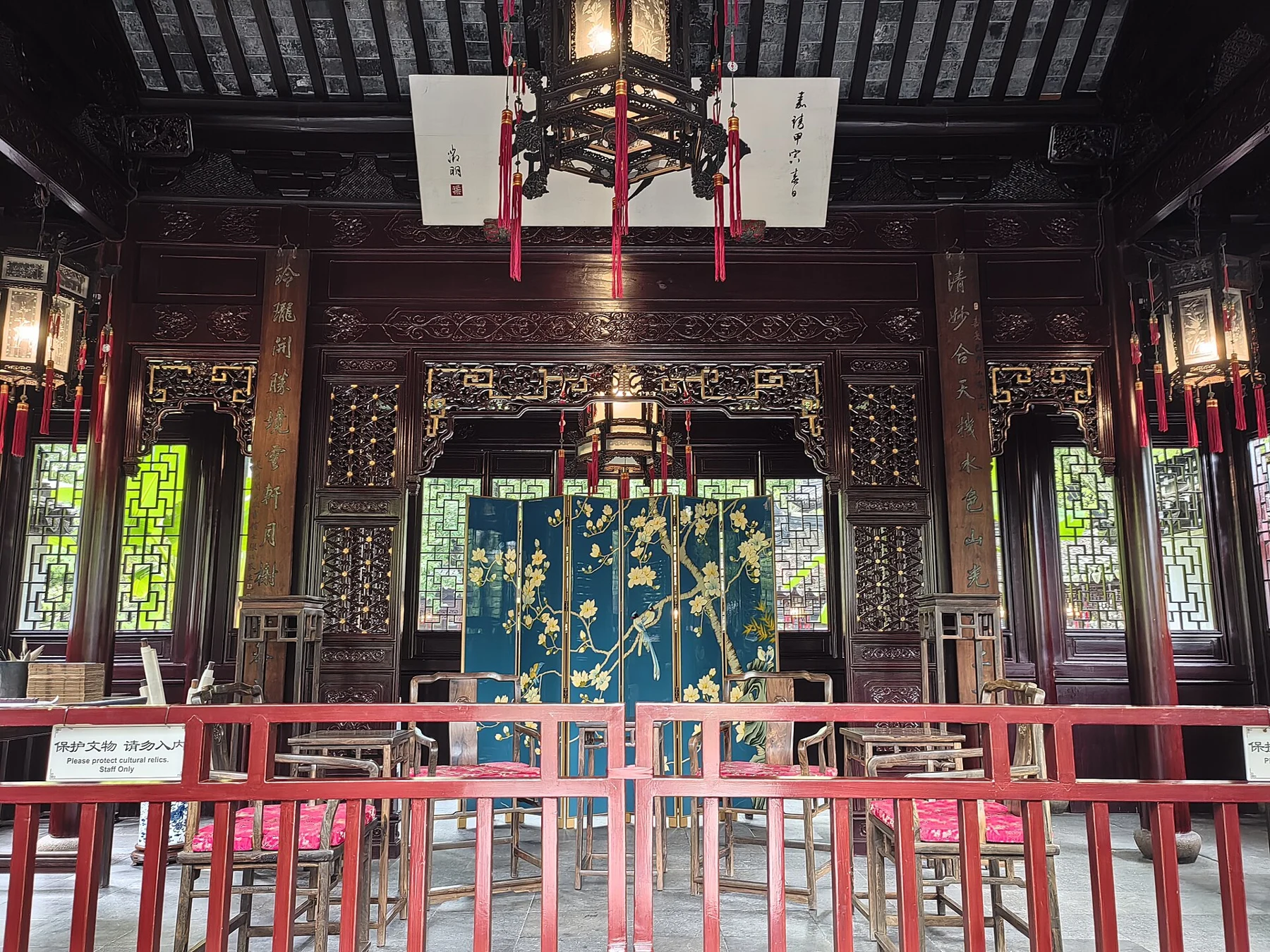 An interior with dark timber beams, a hanging lantern, red railings and an inscribed plaque.