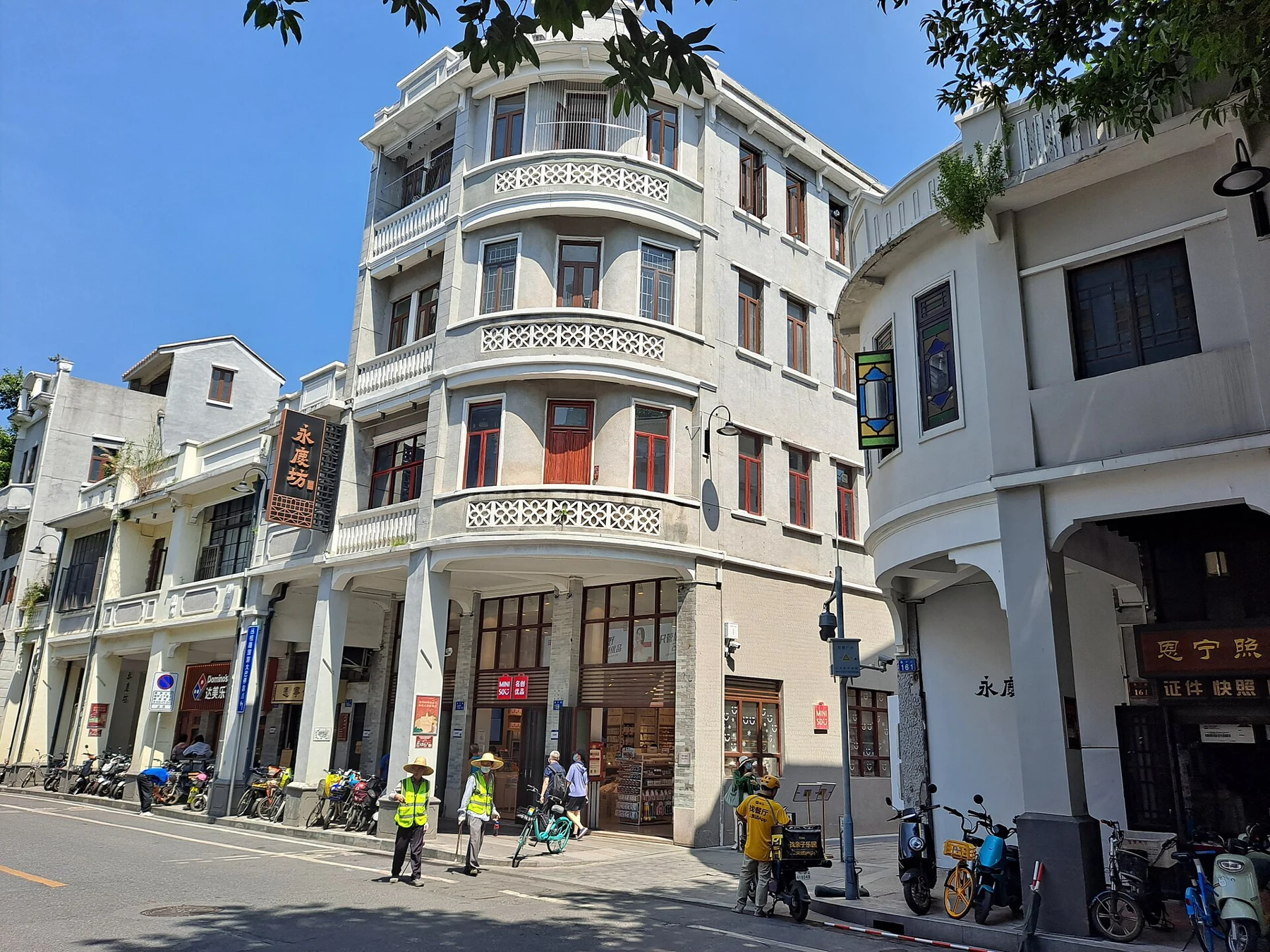Pale rounded corner building with stacked balconies and different-coloured shutters.