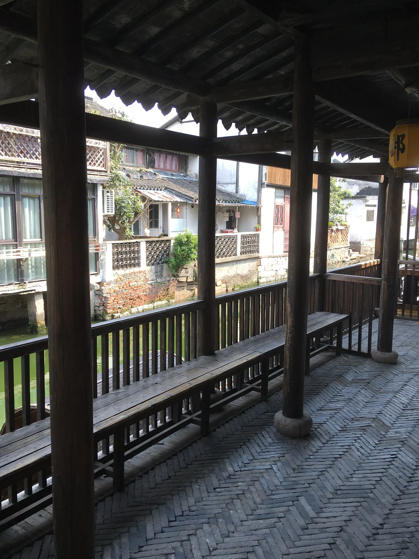 Dark timber columns and railings above a stone floor beside a narrow canal.