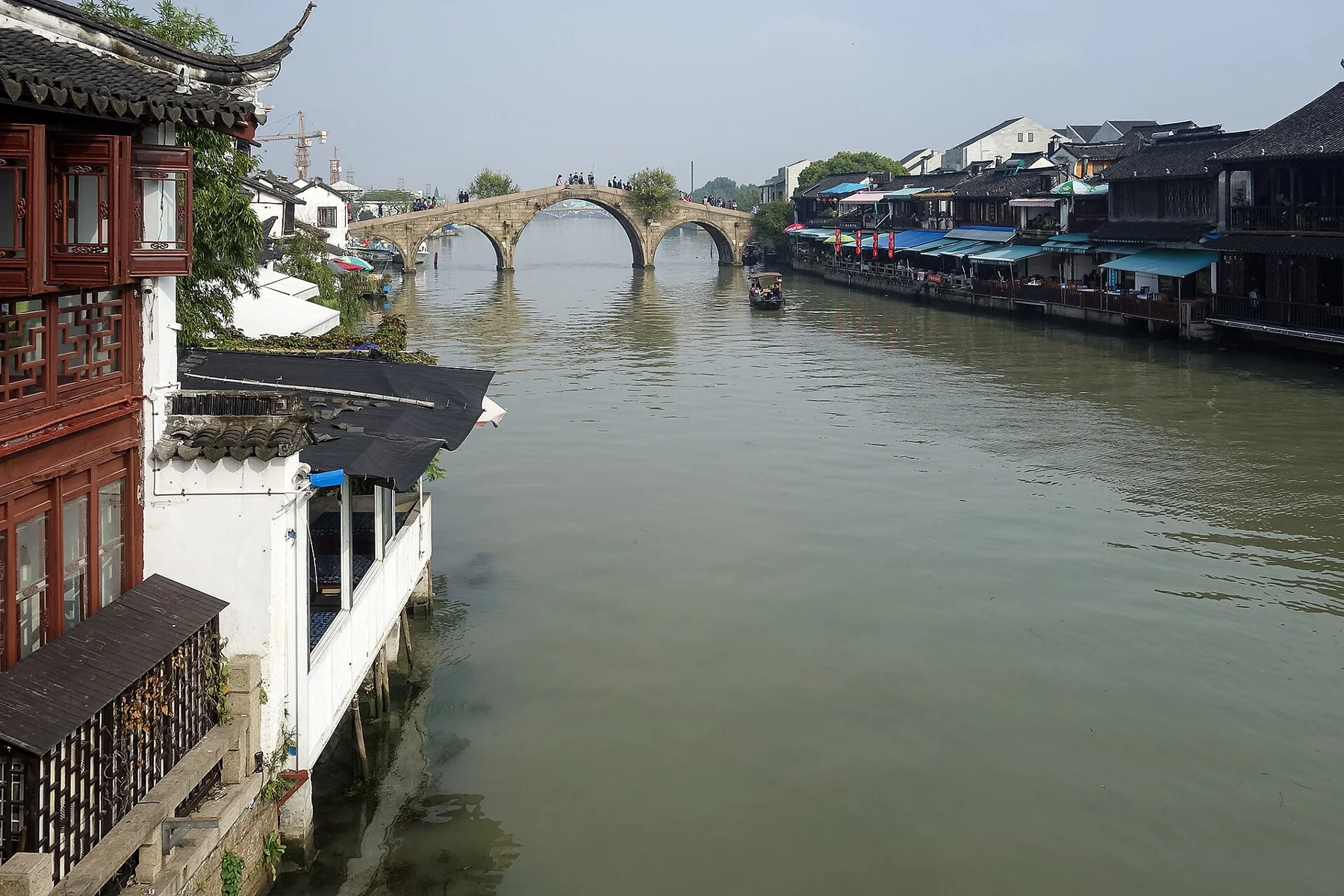 Stone bridge arches spanning a broad river beyond a wooden riverside building.