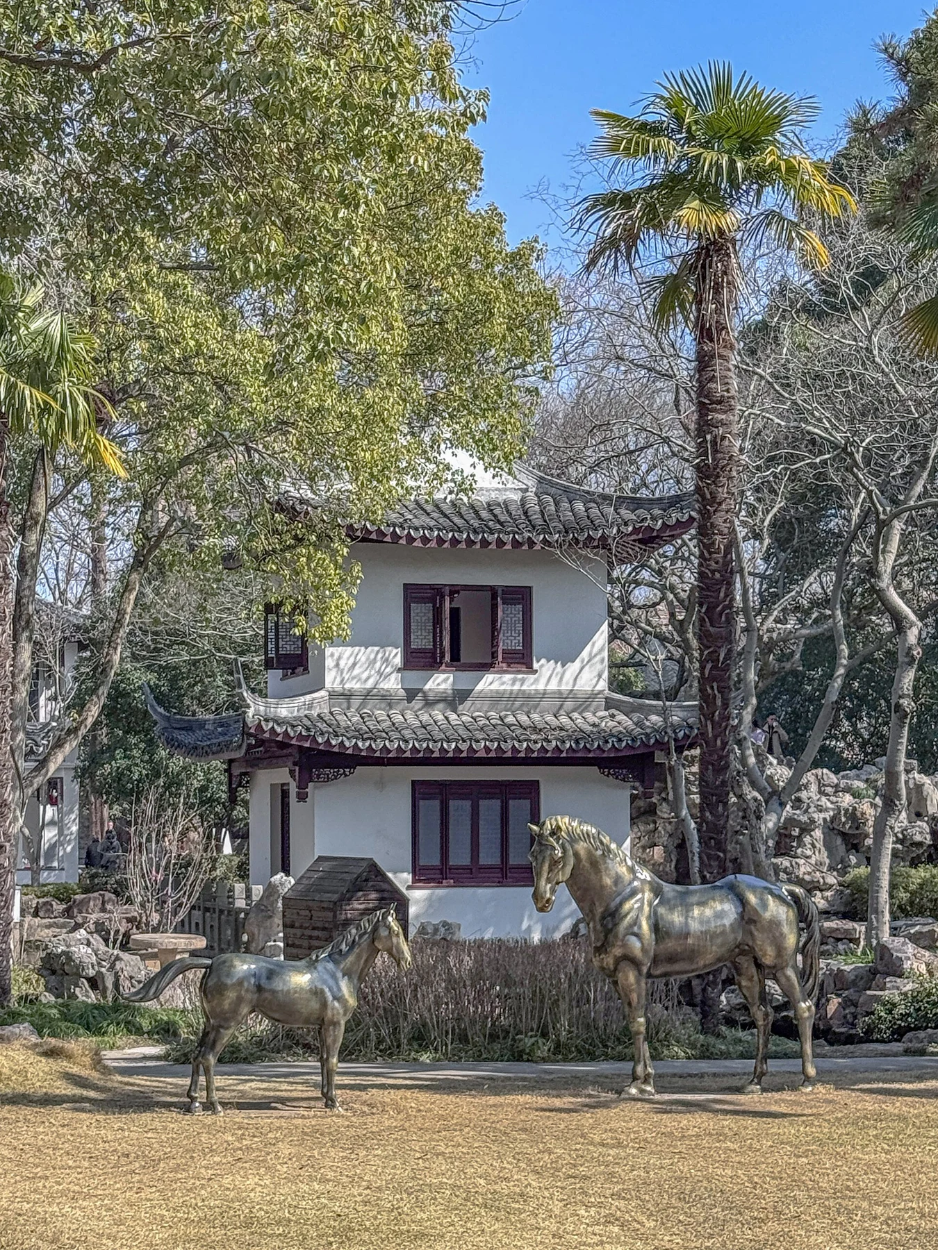 Two horse sculptures in front of a two-storey pavilion among rockwork and trees.