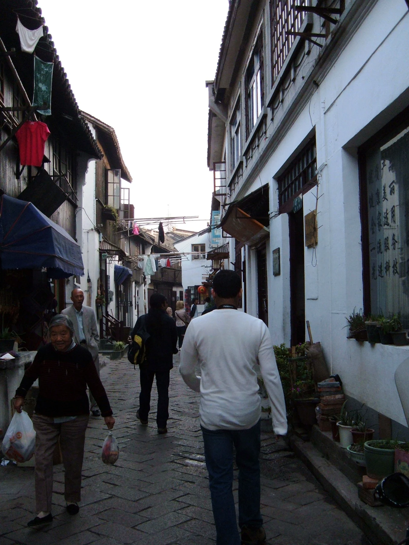 People walking between closely spaced low-rise buildings in a narrow lane.