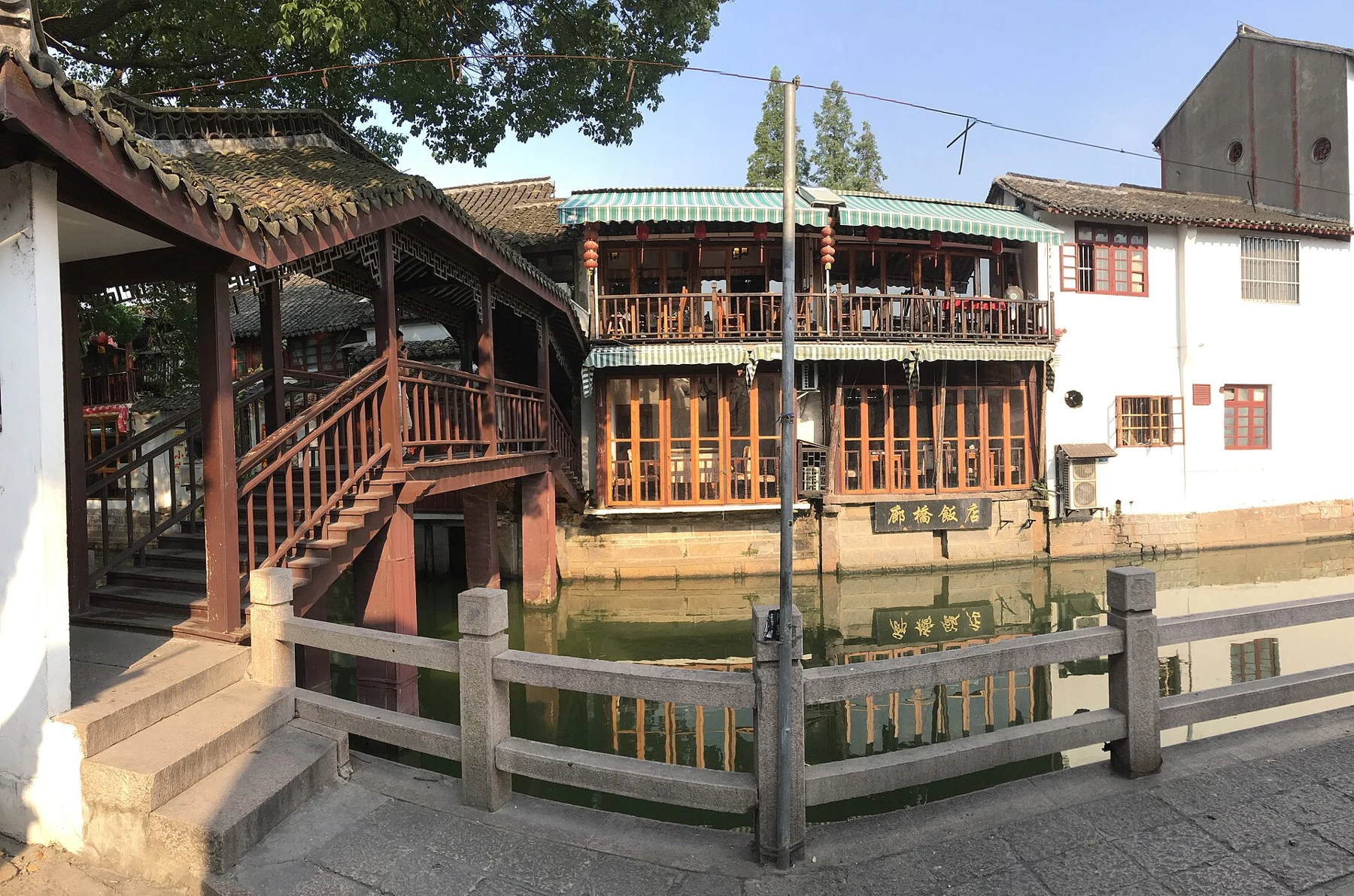 A roofed timber crossing and steps beside a narrow canal and waterside buildings.