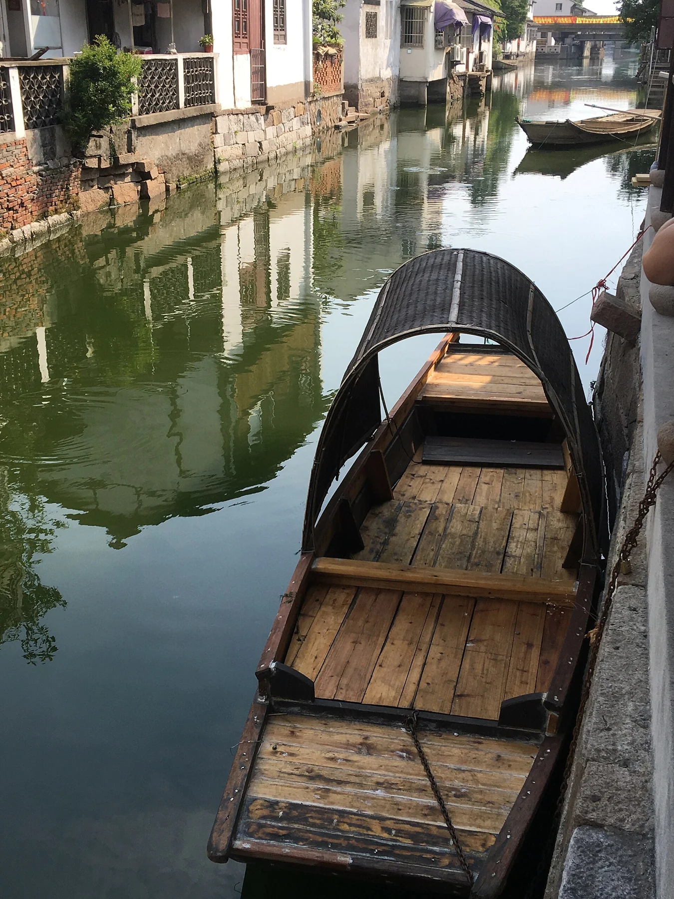 A narrow wooden boat moored beside a stone embankment beneath a small dark canopy.