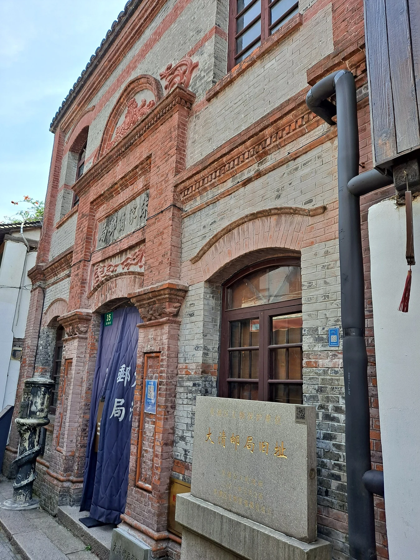 A red-and-grey brick façade with arched openings and a blue hanging doorway curtain.